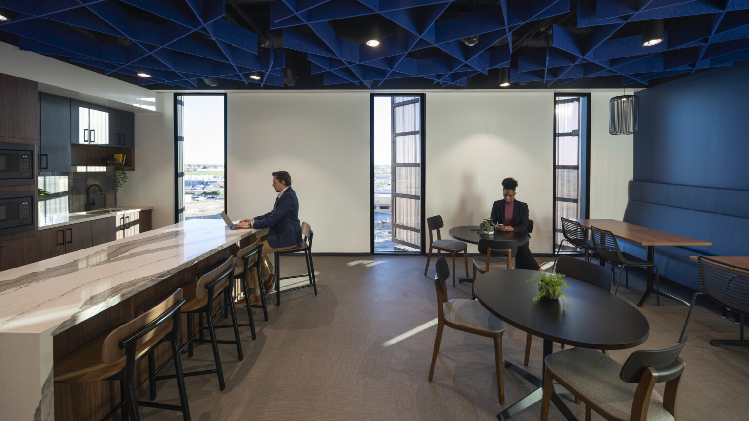 Office common space with blue accent wall and textural ceiling over mixed seating and marble counter, kitchenette left