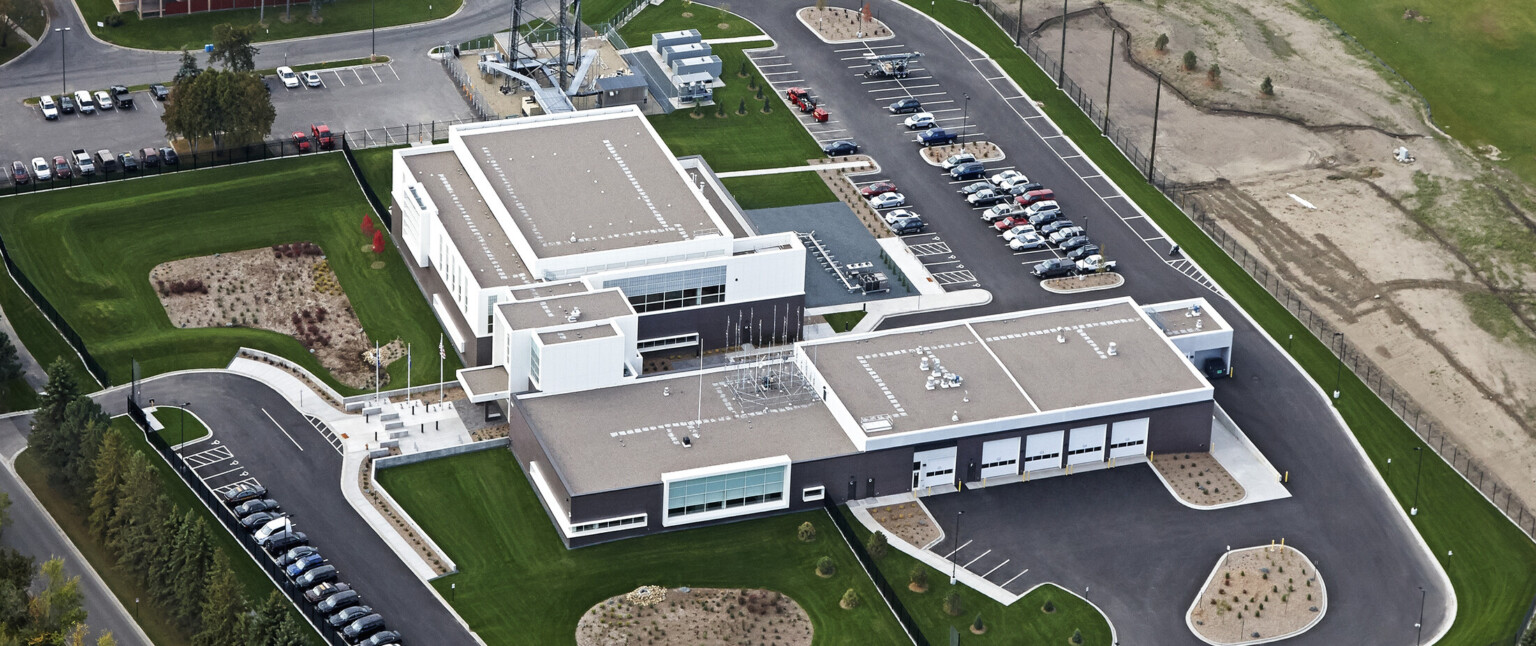 Aerial view of a multistory office building with dark exterior walls with multiple garage doors in the back surrounded by parking lots