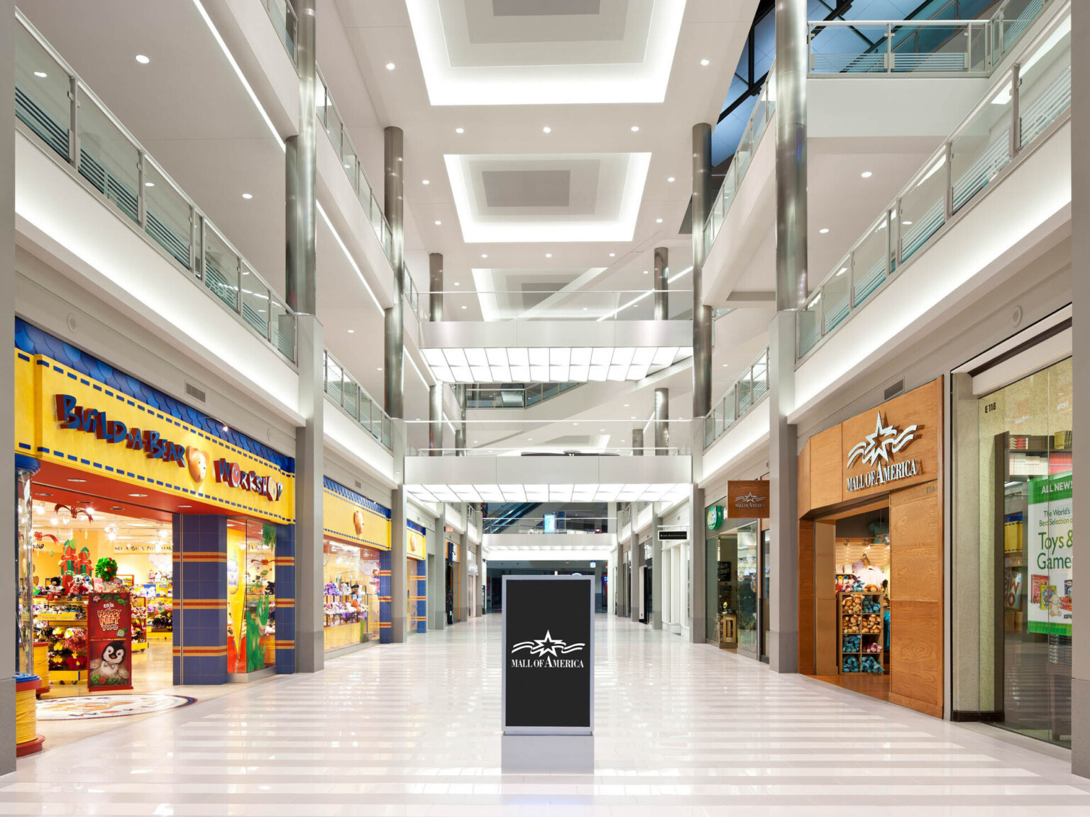 Multilevel mall atrium surrounded by stores with white boxed lighting on the ceiling