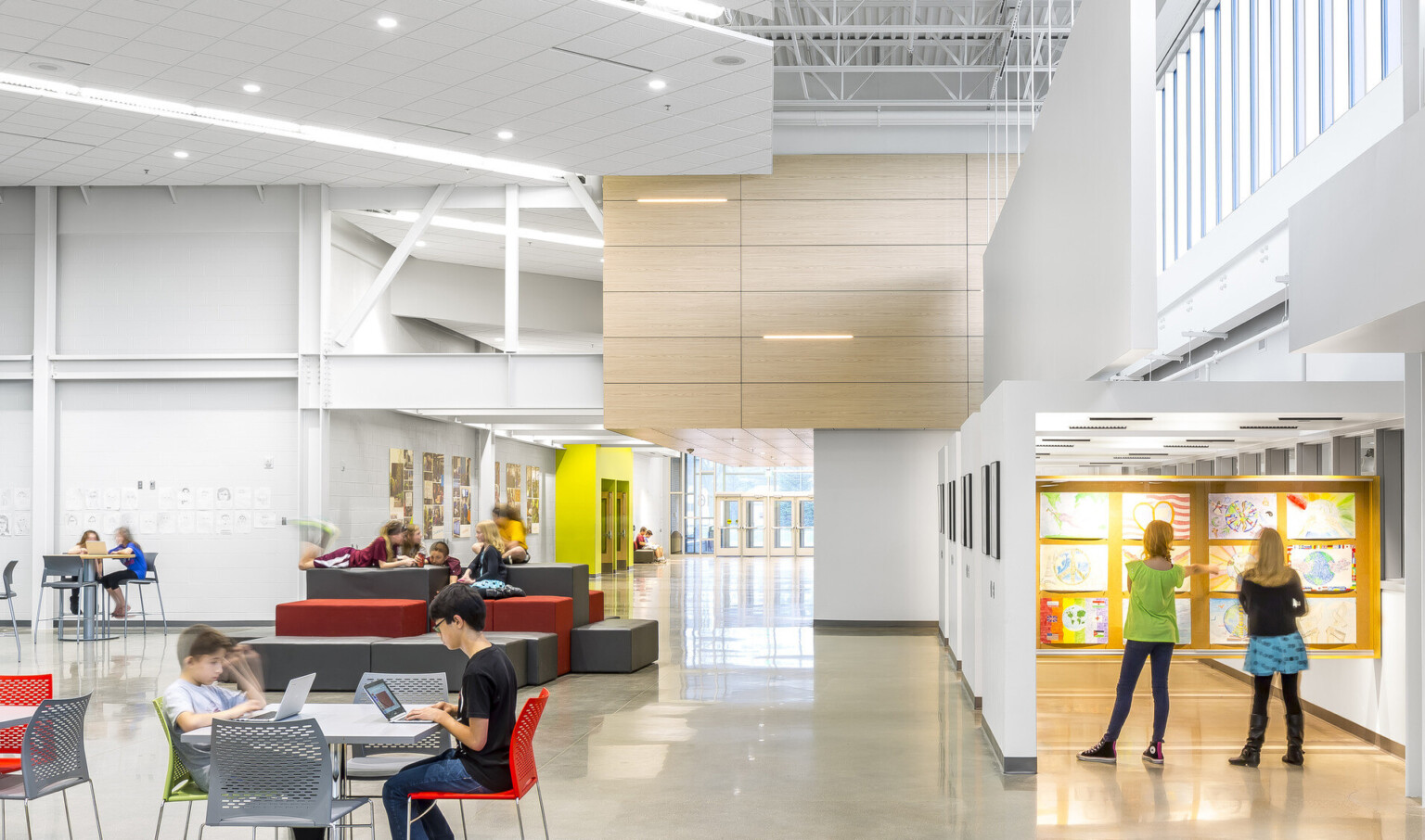 A white room with exposed structural beams. Ergonomic seating. Right, an atrium with art displayed. Wood drop ceiling detail