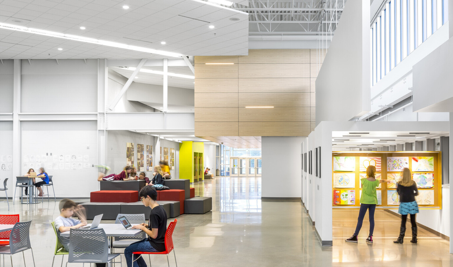 A white room with exposed structural beams. Ergonomic seating. Right, an atrium with art displayed. Wood drop ceiling detail