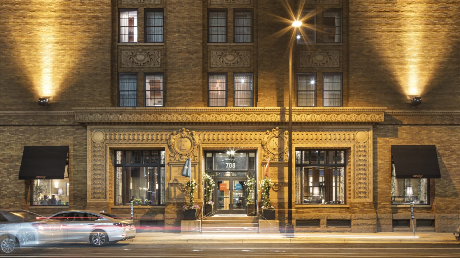 Exterior view of historic mill district cement building with uplighting and ornamental emblems at the Canopy Mill District