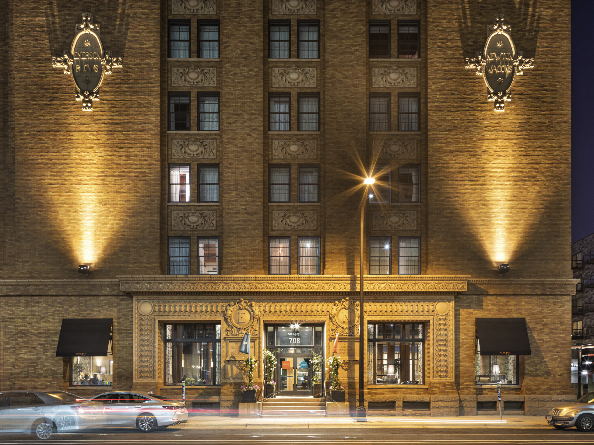 Exterior view of historic mill district cement building with uplighting and ornamental emblems at the Canopy Mill District
