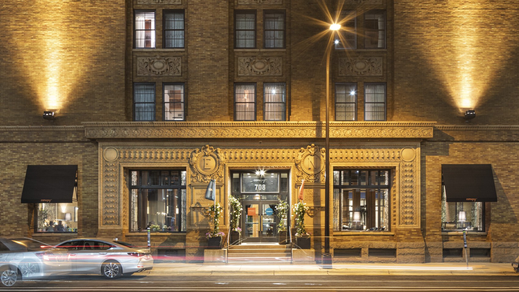Exterior view of historic mill district cement building with uplighting and ornamental emblems at the Canopy Mill District