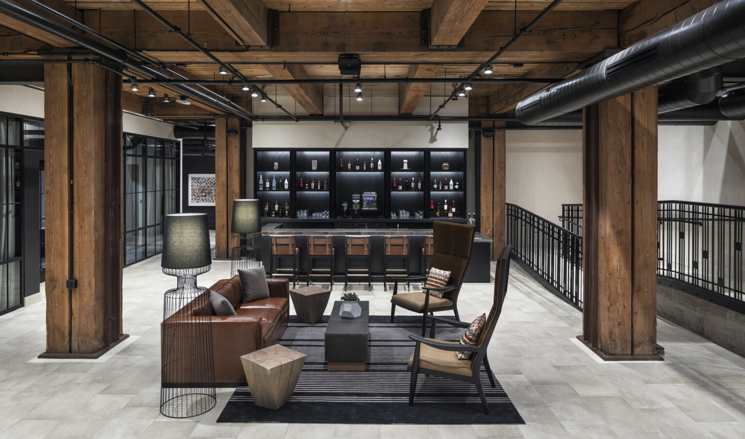 Comfortable seating in front of black bar in white room with wood ceiling, beams, and columns. Black metal railing to right