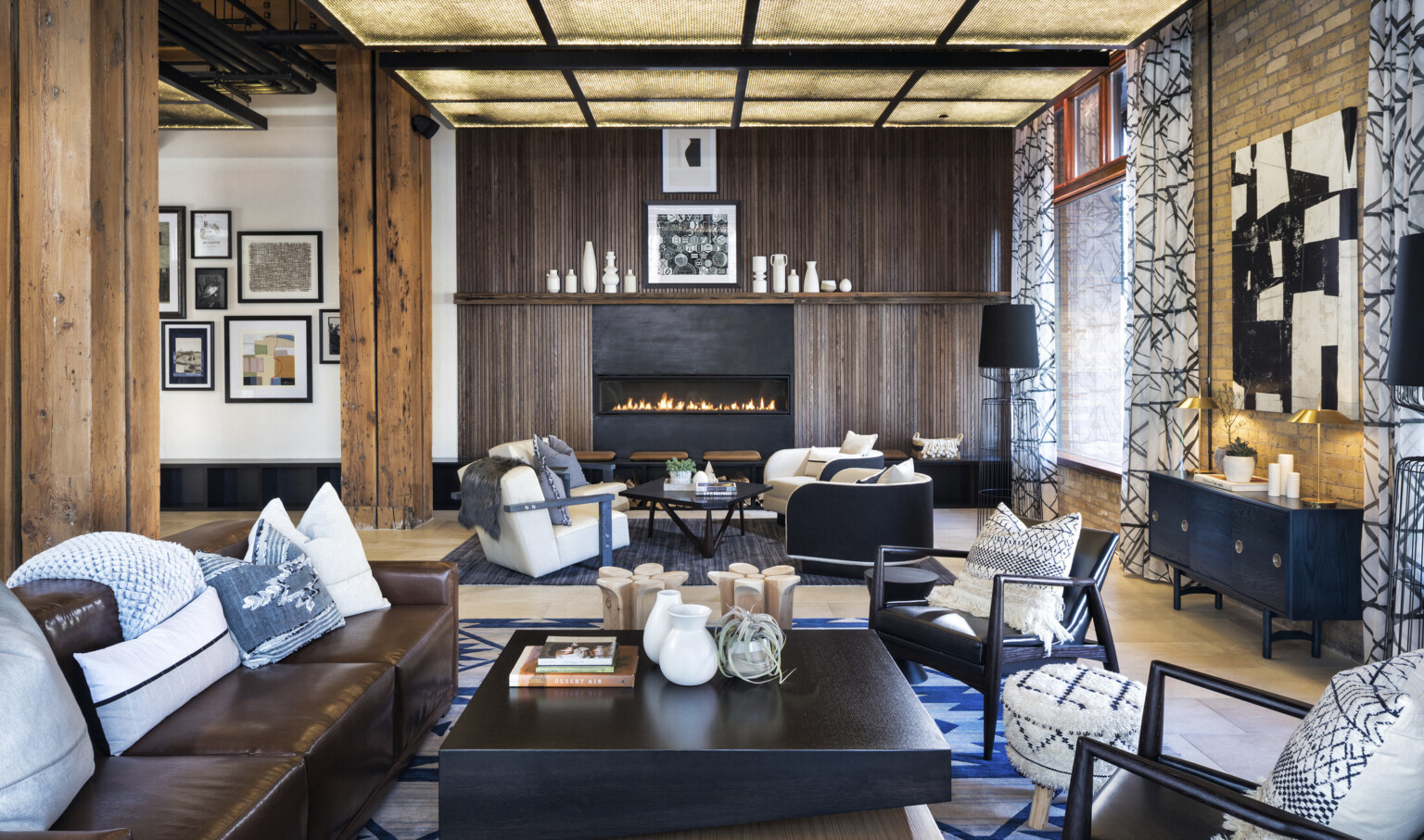 Seating area with arm chairs and couches in front of wood fireplace in white room with large curtained window