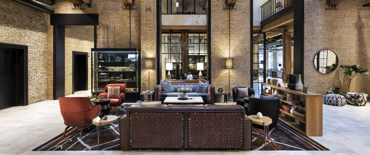 Interior atrium with exposed brick. Seating area at center and wood beams overhead. 2 walkways on sides above with metal rail