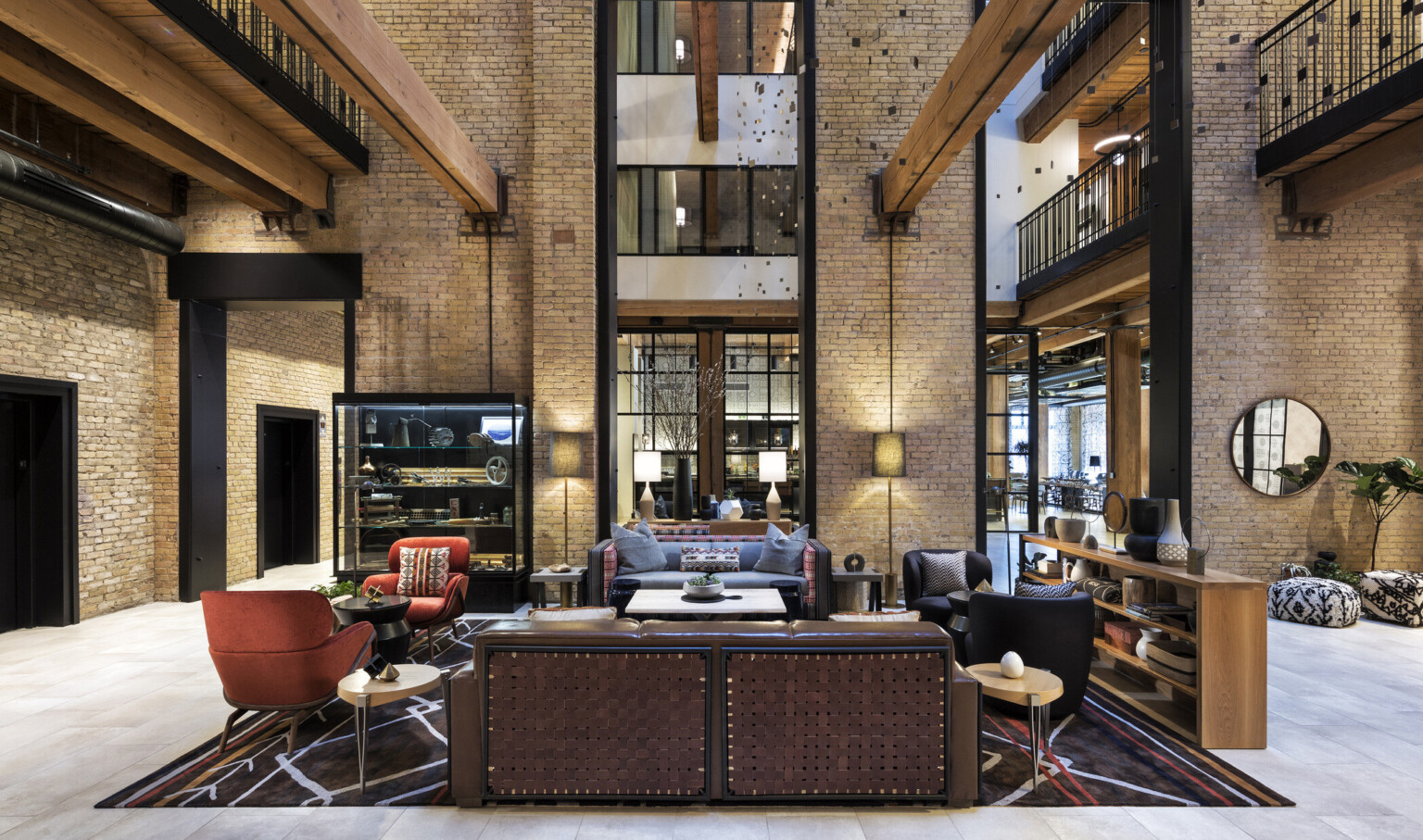 Interior atrium with exposed brick. Seating area at center and wood beams overhead. 2 walkways on sides above with metal rail