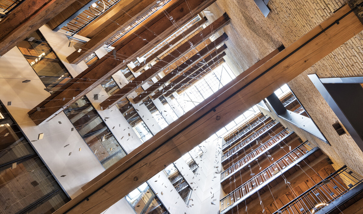 View of multistory atrium from above with walkways at each levels and wood beams between. Strung squares hang from grid above View of multistory atrium from above with walkways at each levels and wood beams between. Strung squares hang from grid above