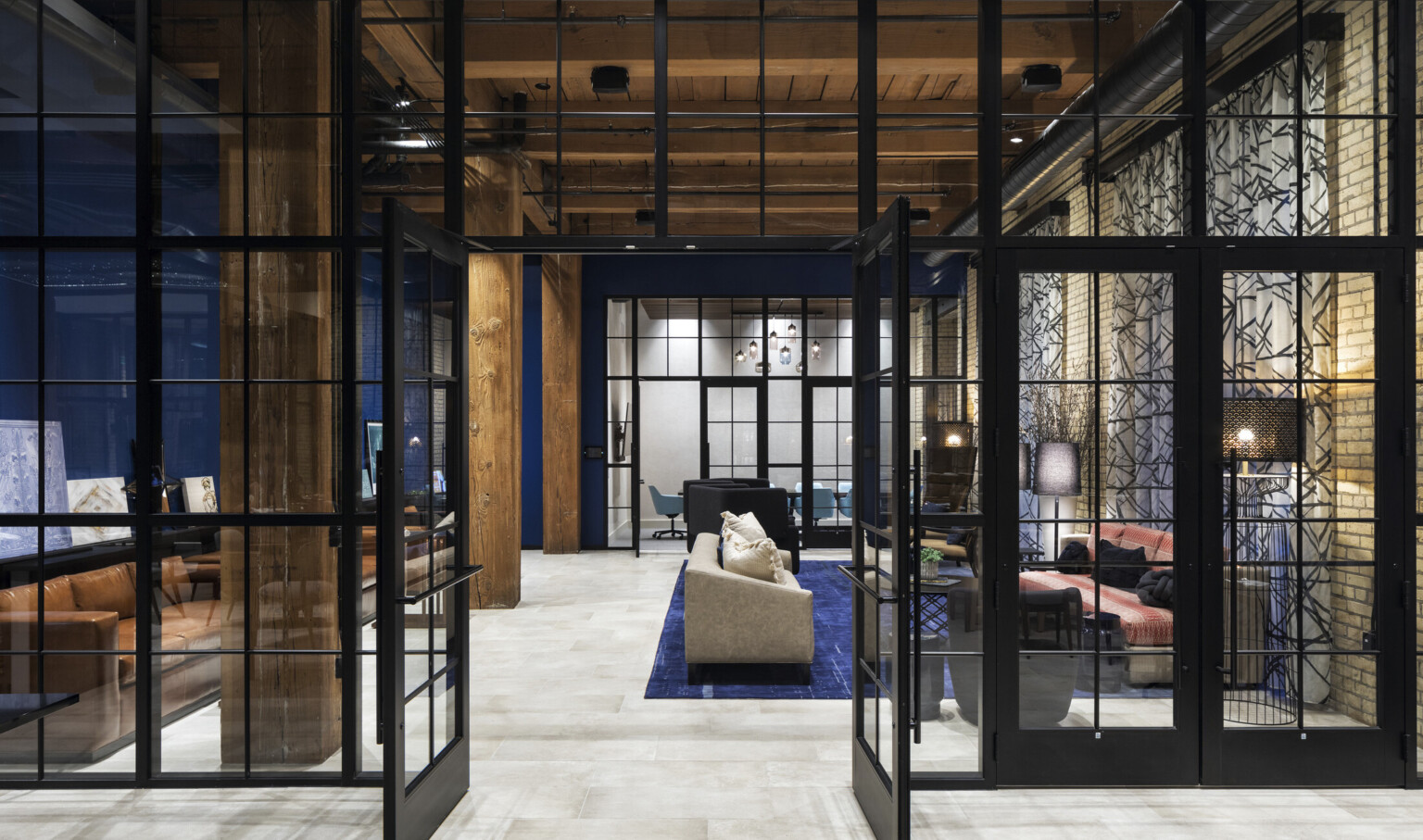 Blue room with wood columns and ceiling of sitting room with couches on blue rug. Glass wall to conference room beyond.