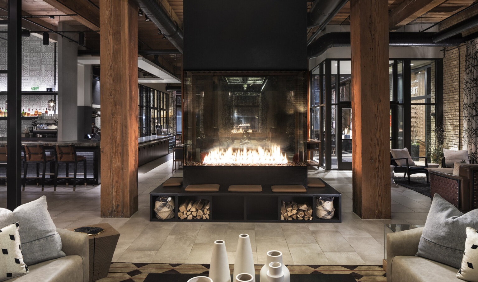 Fireplace elevated on black bench with under seat storage between wood pillars in bar with floor to ceiling windows