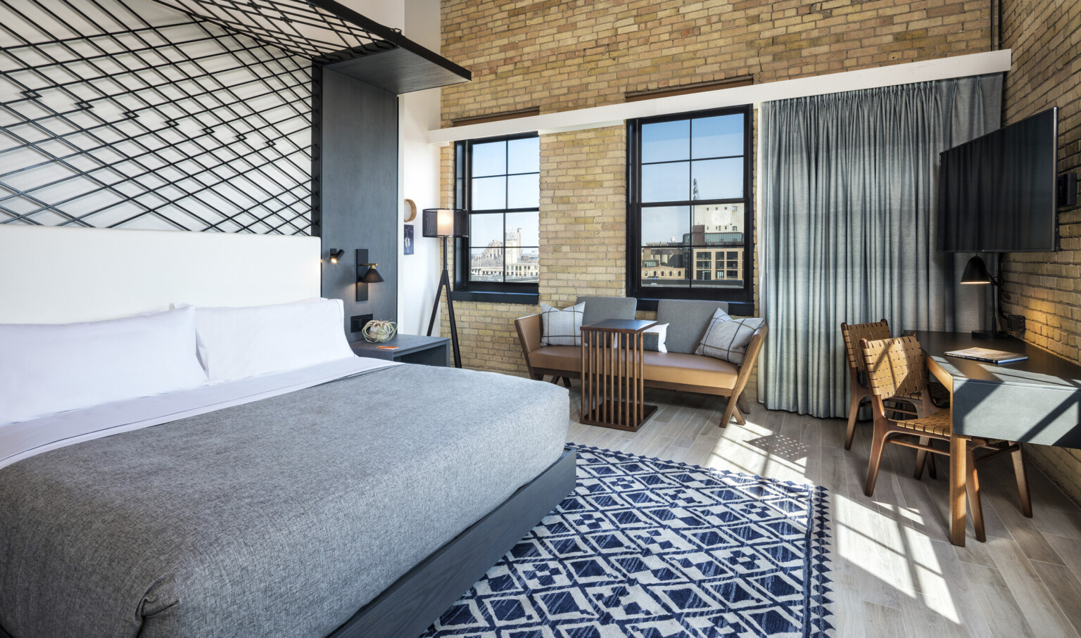 Guest room with exposed brick wall. Bed with white headboard against black metallic grid anchored to grey wall accent