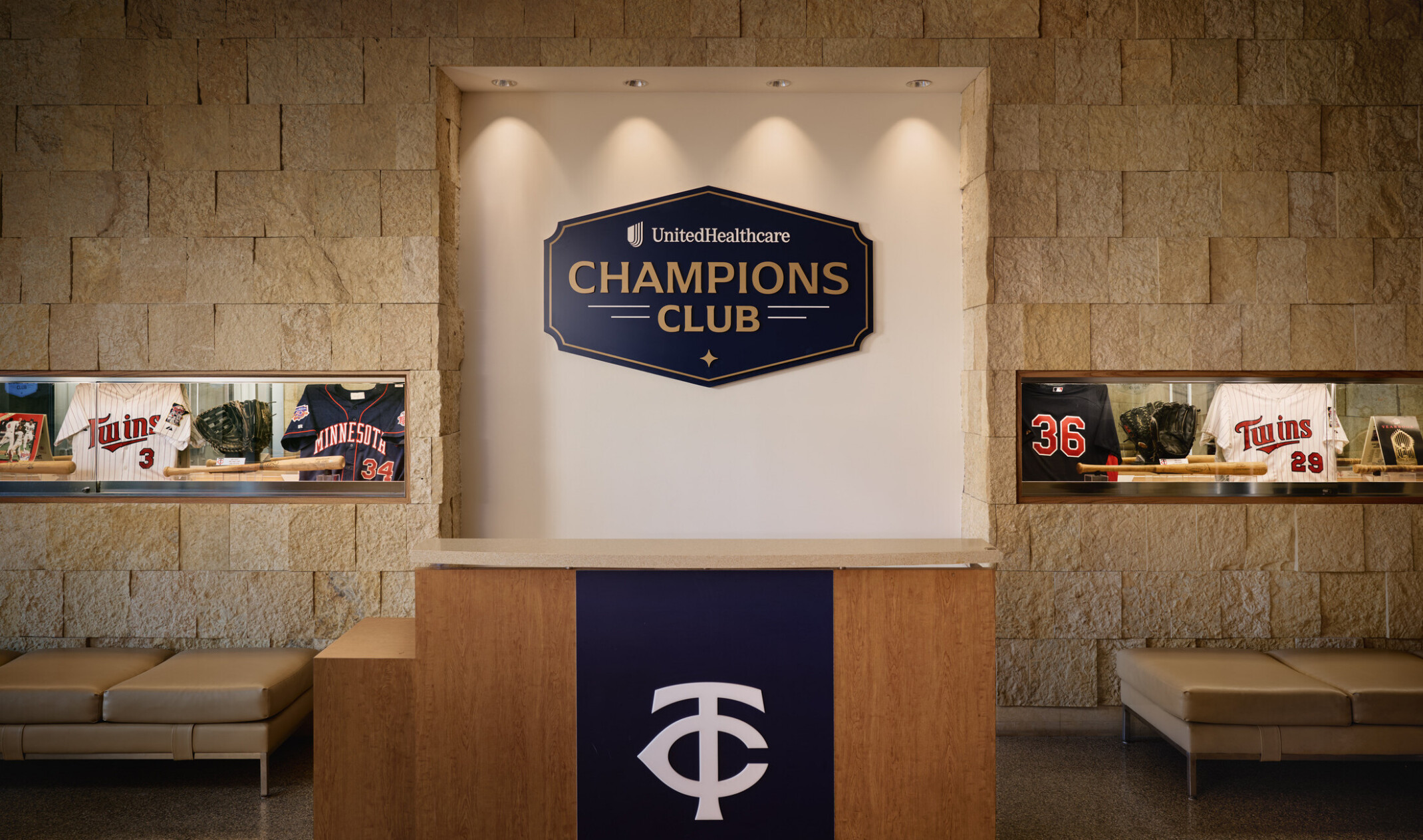 Reception area for the UnitedHealthcare Champions Club featuring Minnesota Twins memorabilia displays, a branded welcome desk, and a stone accent wall with illuminated club signage.