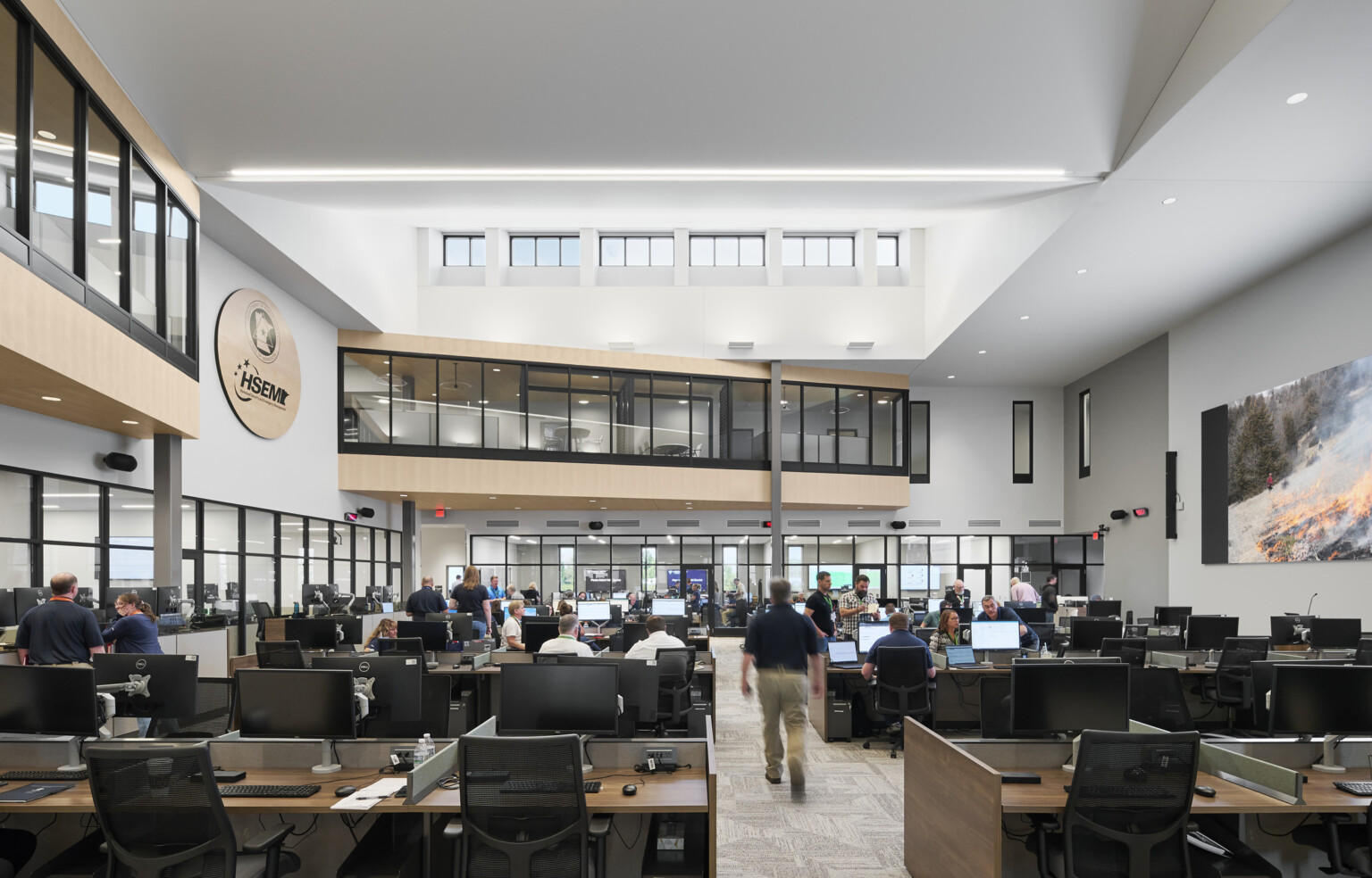 interior photo; a busy open office filled with people working at desks with computers and monitors; high ceilings with skylights, and glass-walled second-floor hallways overlook the main work area below