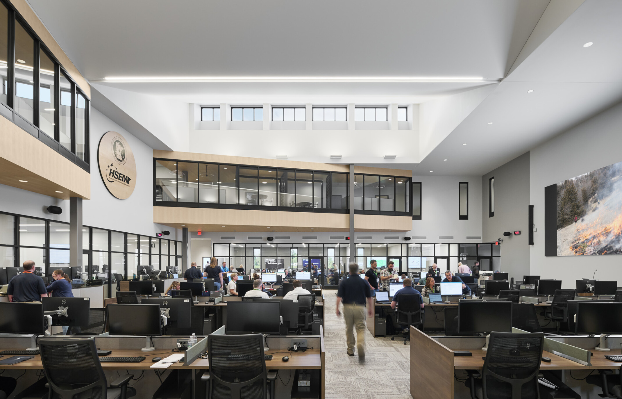 interior photo; a busy open office filled with people working at desks with computers and monitors; high ceilings with skylights, and glass-walled second-floor hallways overlook the main work area below