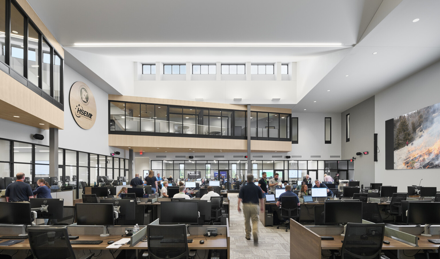interior photo; a busy open office filled with people working at desks with computers and monitors; high ceilings with skylights, and glass-walled second-floor hallways overlook the main work area below