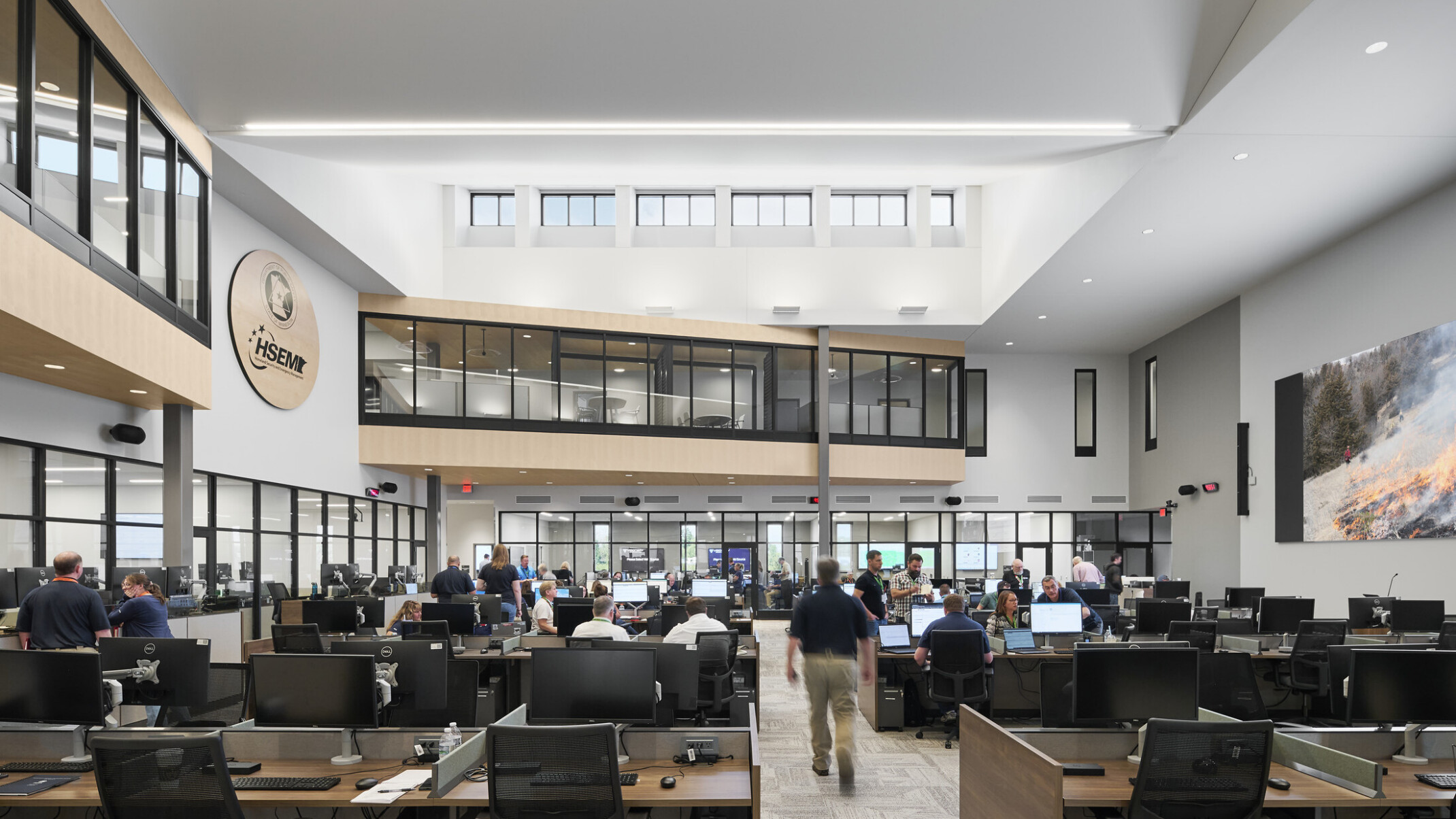 interior photo; a busy open office filled with people working at desks with computers and monitors; high ceilings with skylights, and glass-walled second-floor hallways overlook the main work area below