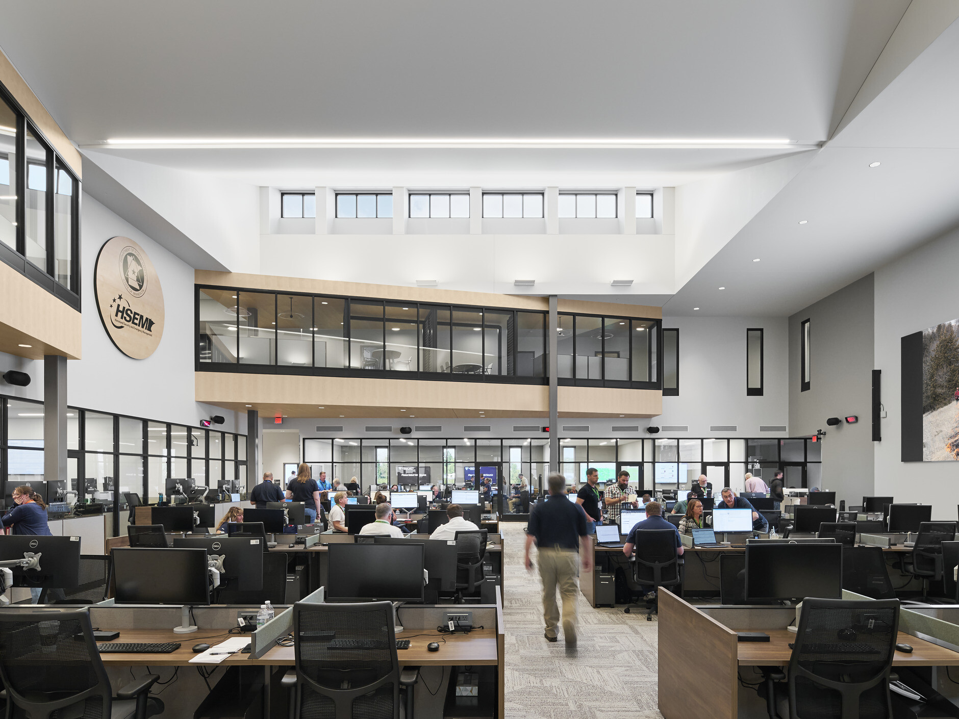 interior photo; a busy open office filled with people working at desks with computers and monitors; high ceilings with skylights, and glass-walled second-floor hallways overlook the main work area below