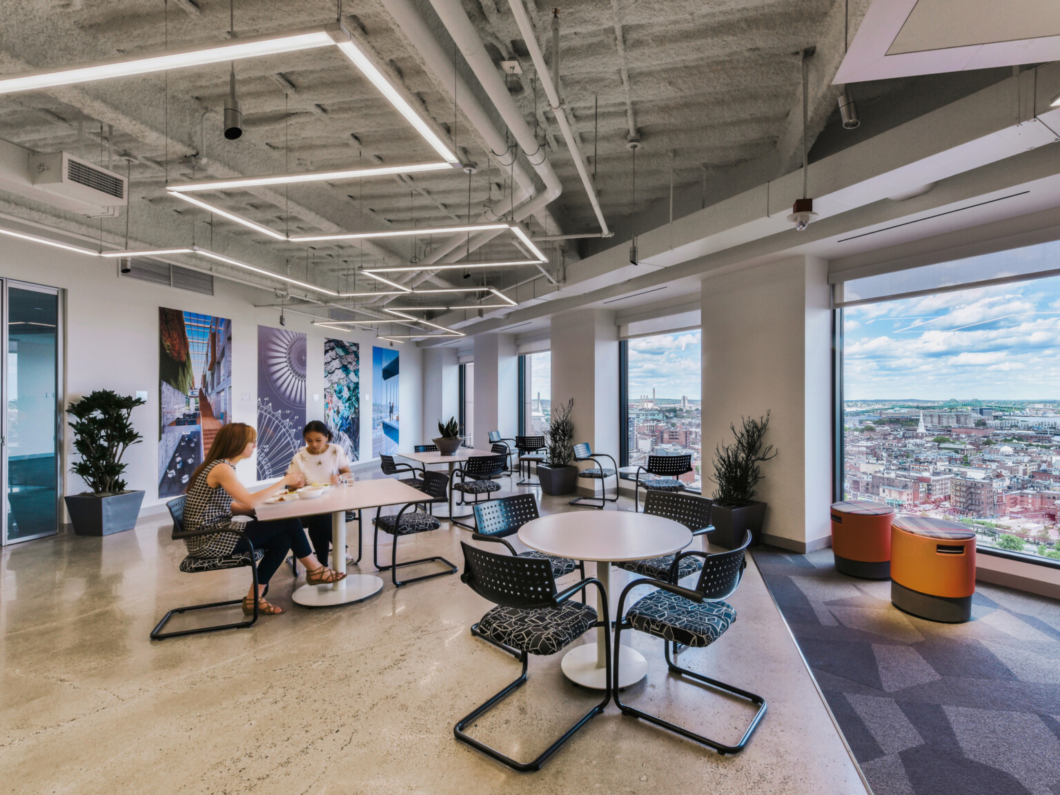 modern office collaboration hub with varied seating and people working at tables in front of floor to ceiling windows; DLR Group Boston office