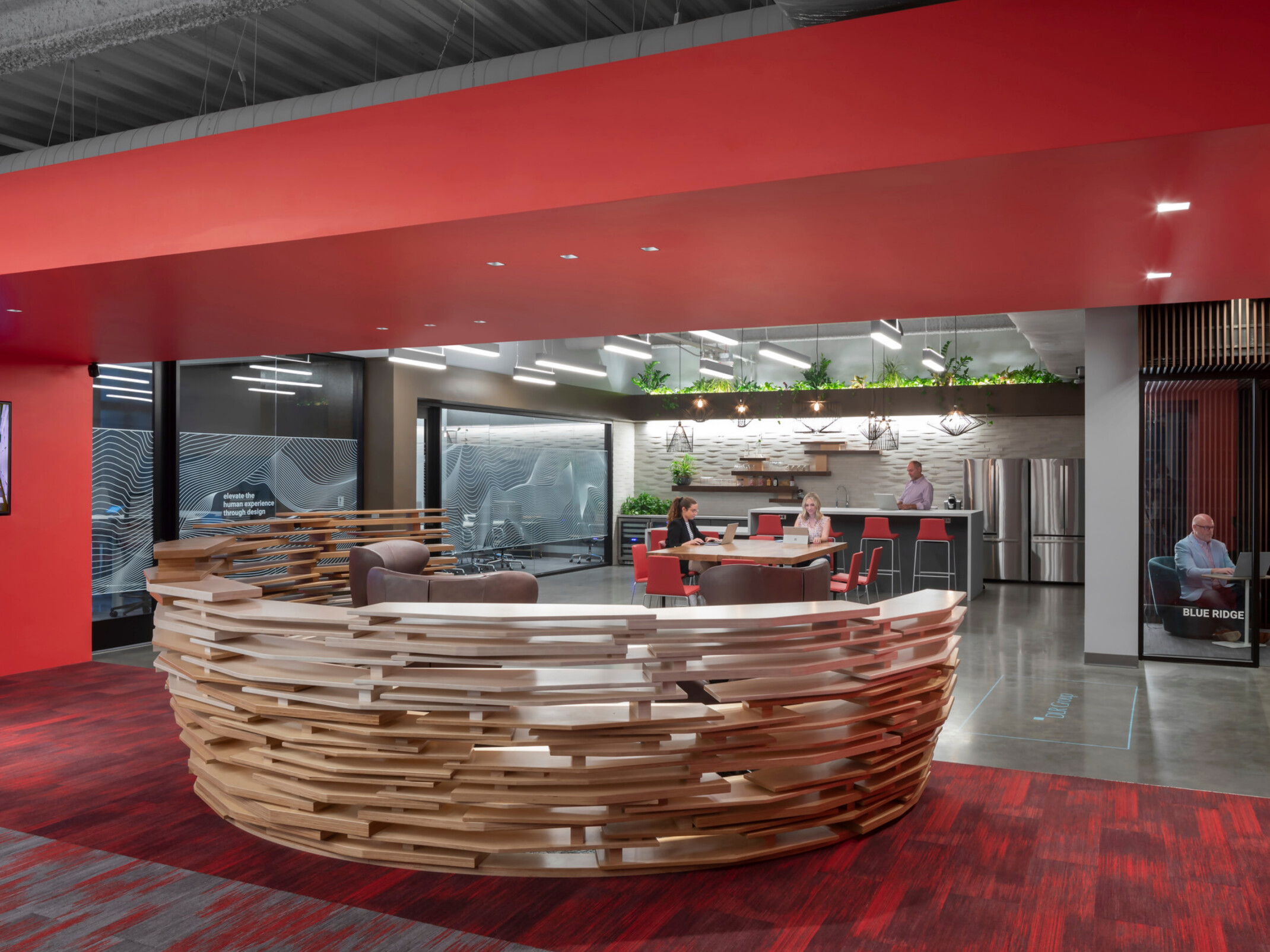 modern office front entrance desk with community collaboration space in the background; front desk surrounded by red walls and carpeting; DLR Group Charlotte office