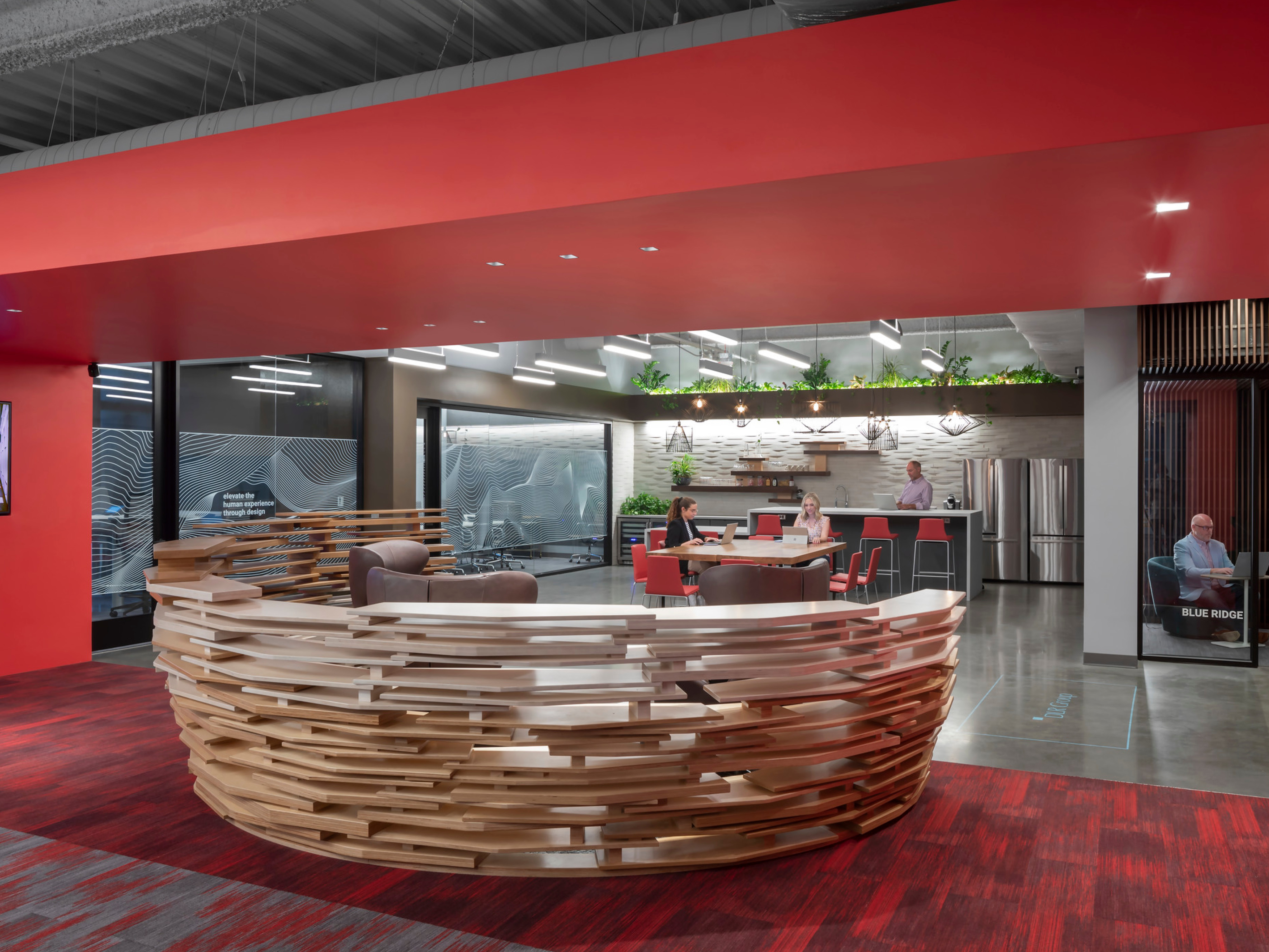 modern office front entrance desk with community collaboration space in the background; front desk surrounded by red walls and carpeting; DLR Group Charlotte office