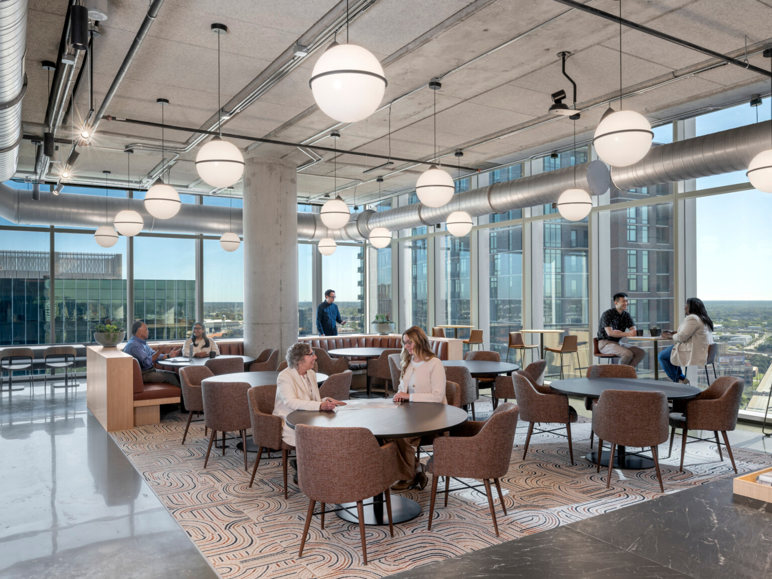 modern office collaboration hub with varied seating and people working at tables, booths and high tops in front of floor to ceiling windows; DLR Group Dallas office