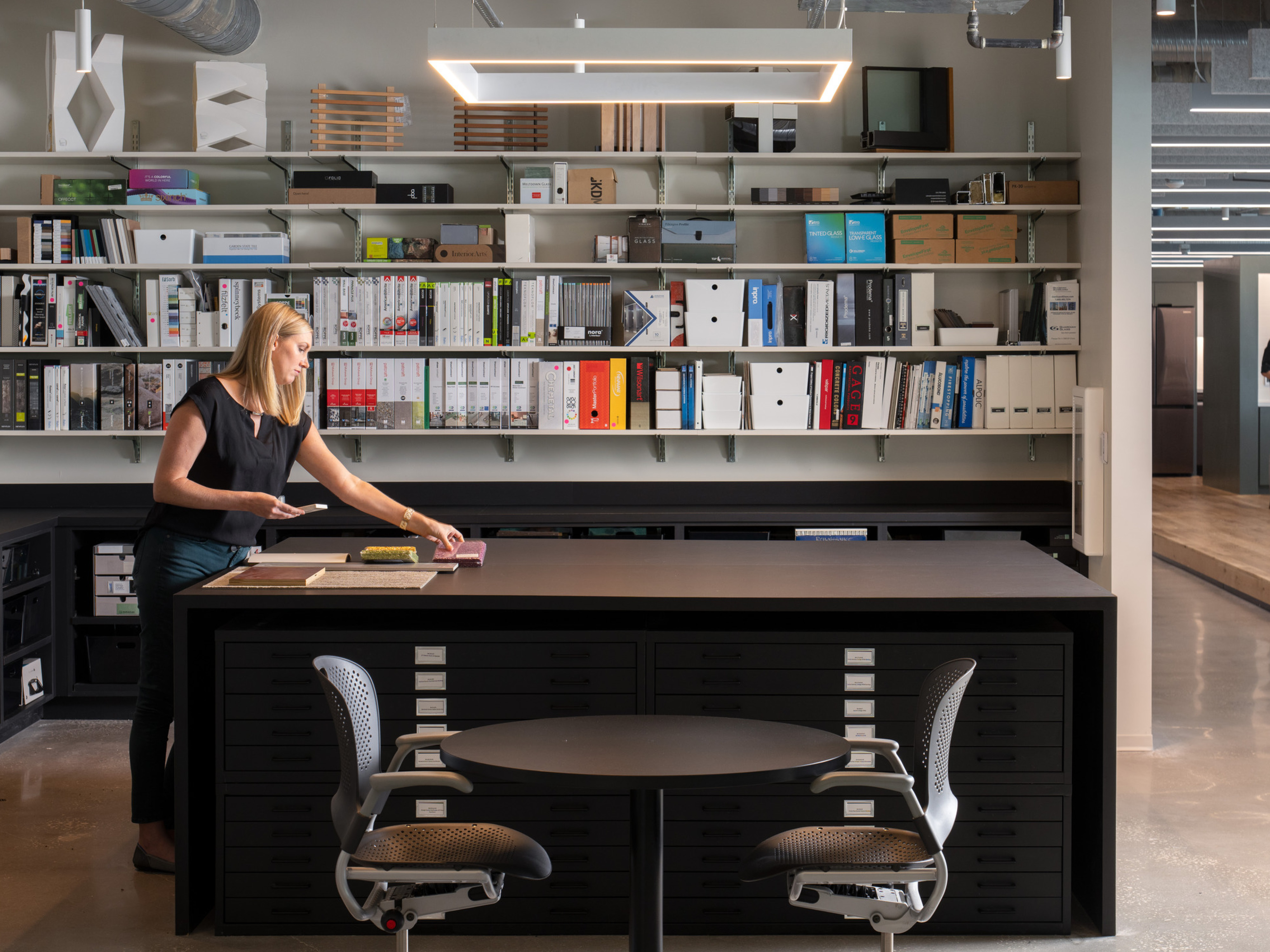 woman standing in a interiors material library at a high top table; DLR Group Orlando office