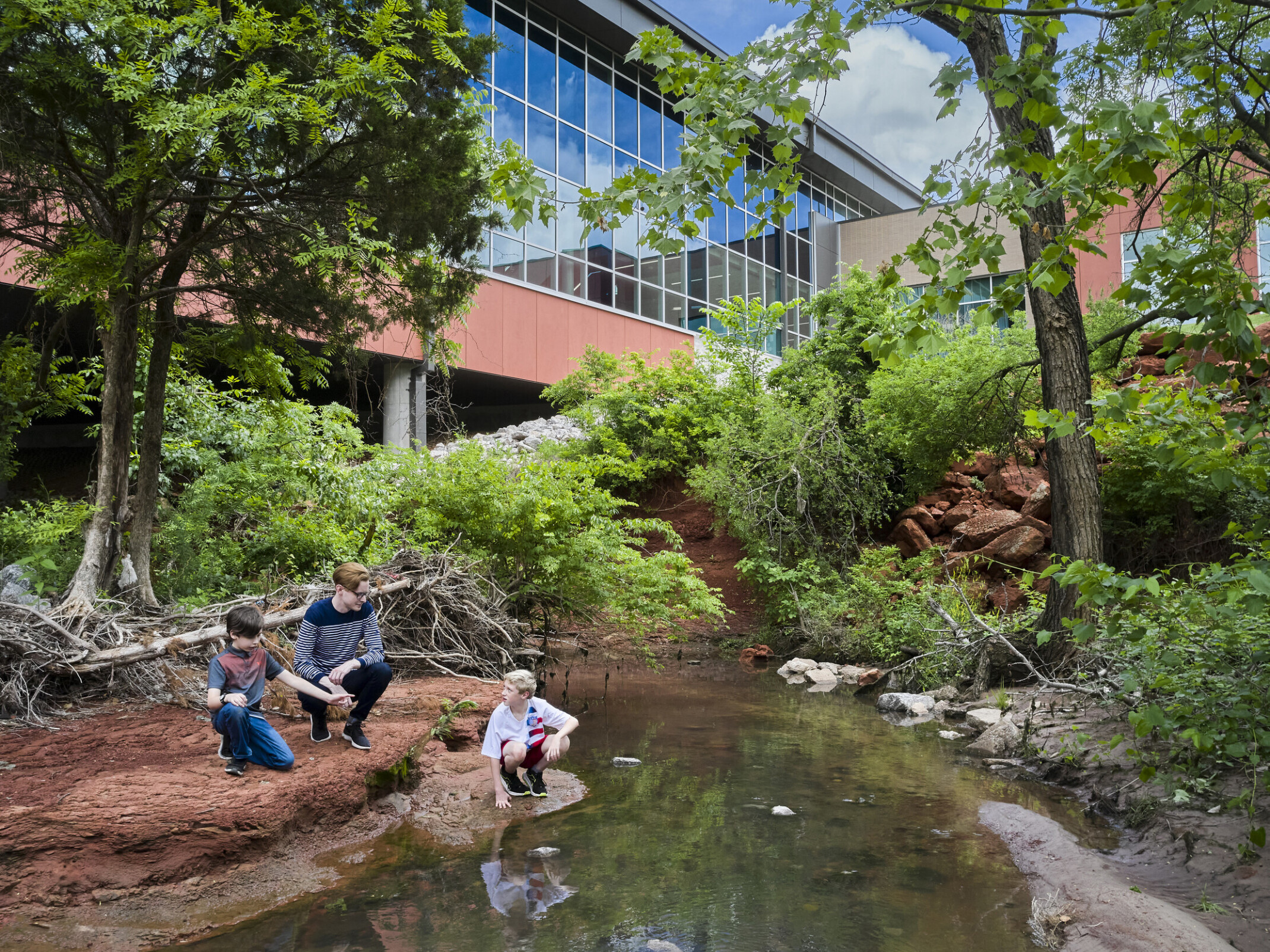 Small creek surrounded by wooded area beside the windowed hallway