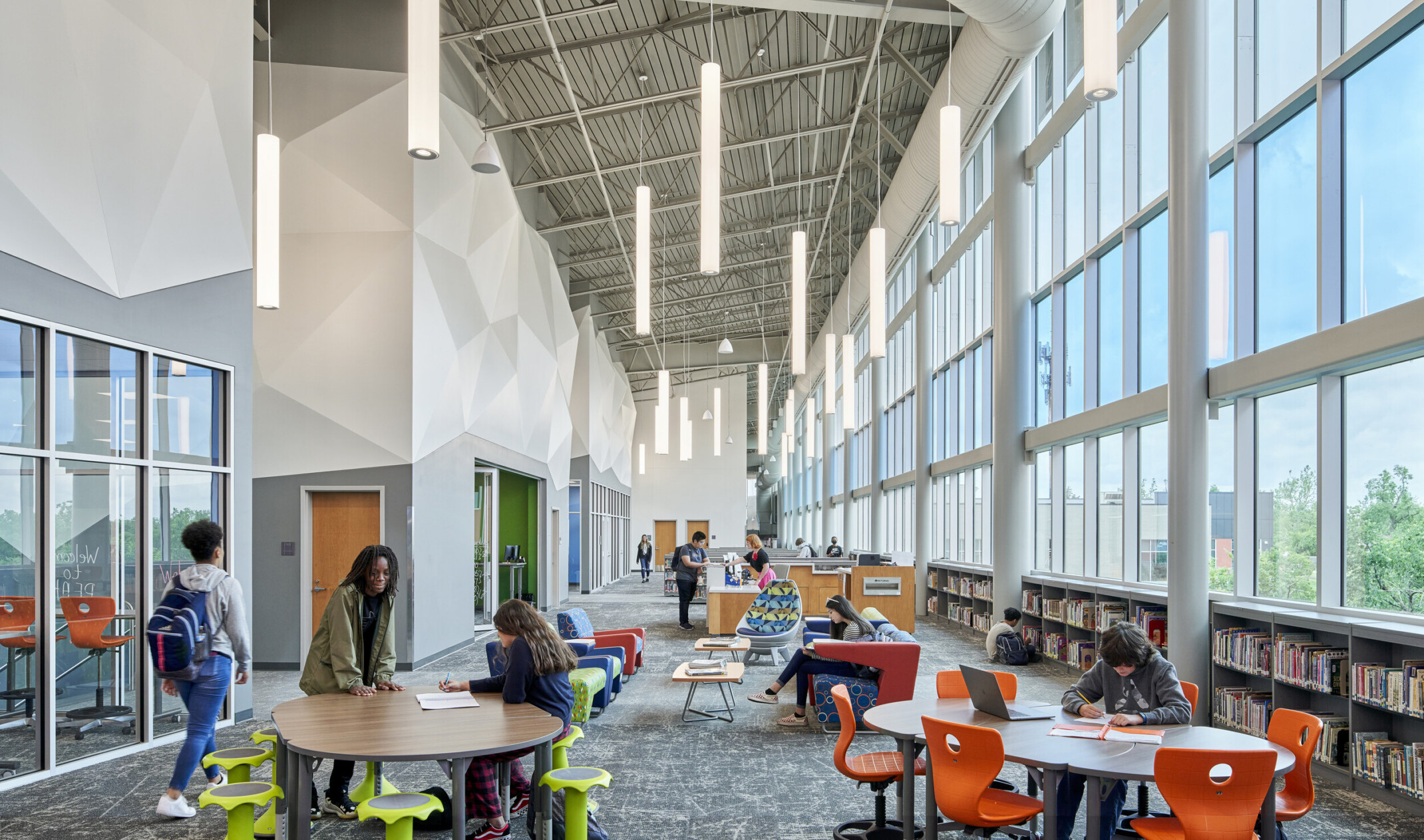 Hallway with double height windows, right, above low book shelves. Left, rooms under white organic sculptures. Seats between