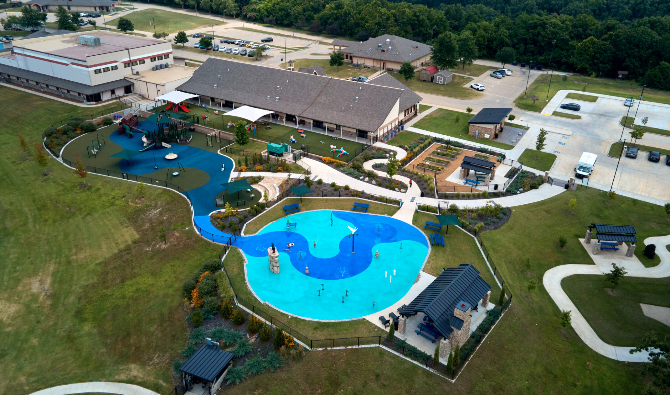 Aerial view of a school playground and building; large bright blue circular play splash space with paths down to school