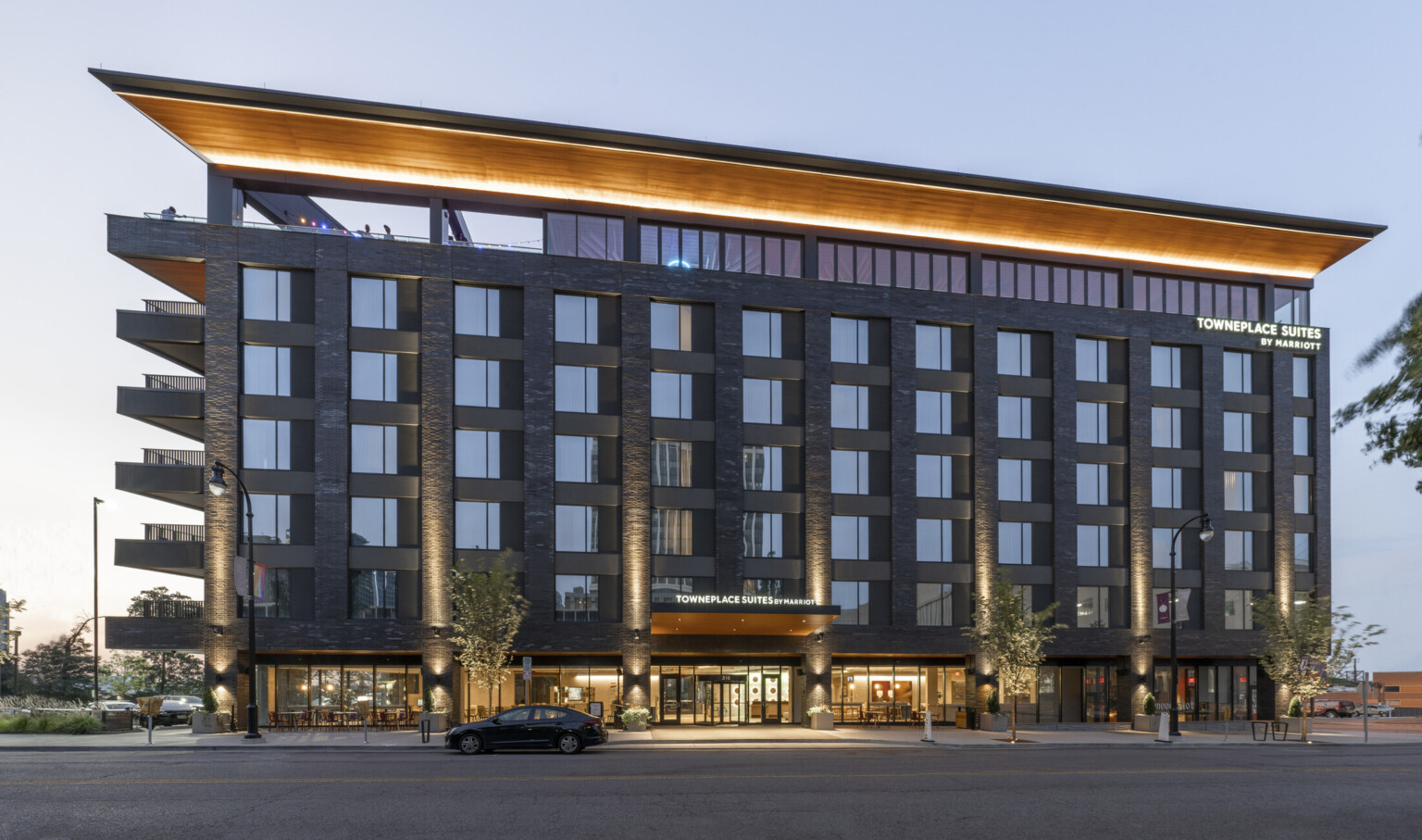 The Towneplace Suites Nashville Downtown seen from street level features assorted tones of gray stone scaling the sides while a warm, honey wood ceiling runs the length of the roof deck.