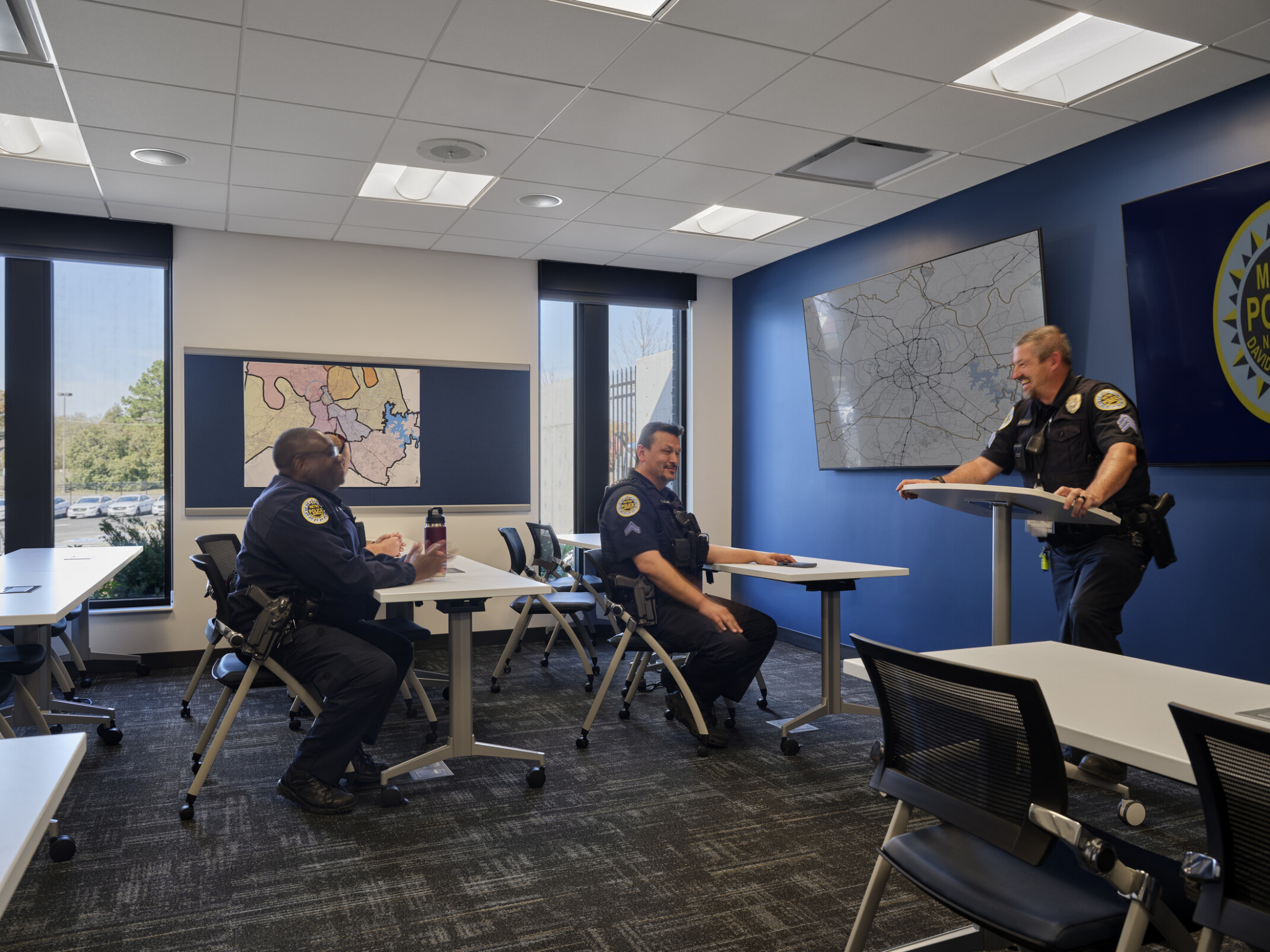 police officers in a classroom meeting space with maps on the walls