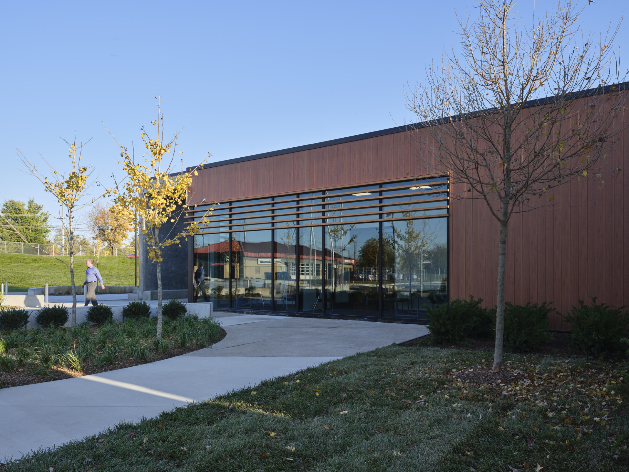 side view of a modern precinct, office building; Landscaped walkway at building entry with glass and wood panel