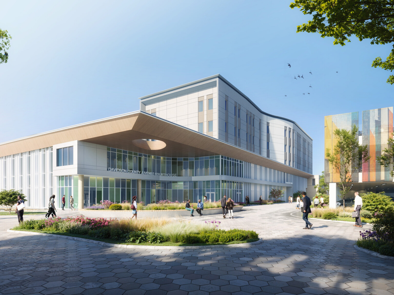 Exterior rendering of the Davidson County Juvenile Courthouse located on the Nashville Youth Center for Empowerment justice campus, with lush landscaping, people passing by, and a view of the new parking structure with multicolored mesh wall panels that enclose the second and third levels.