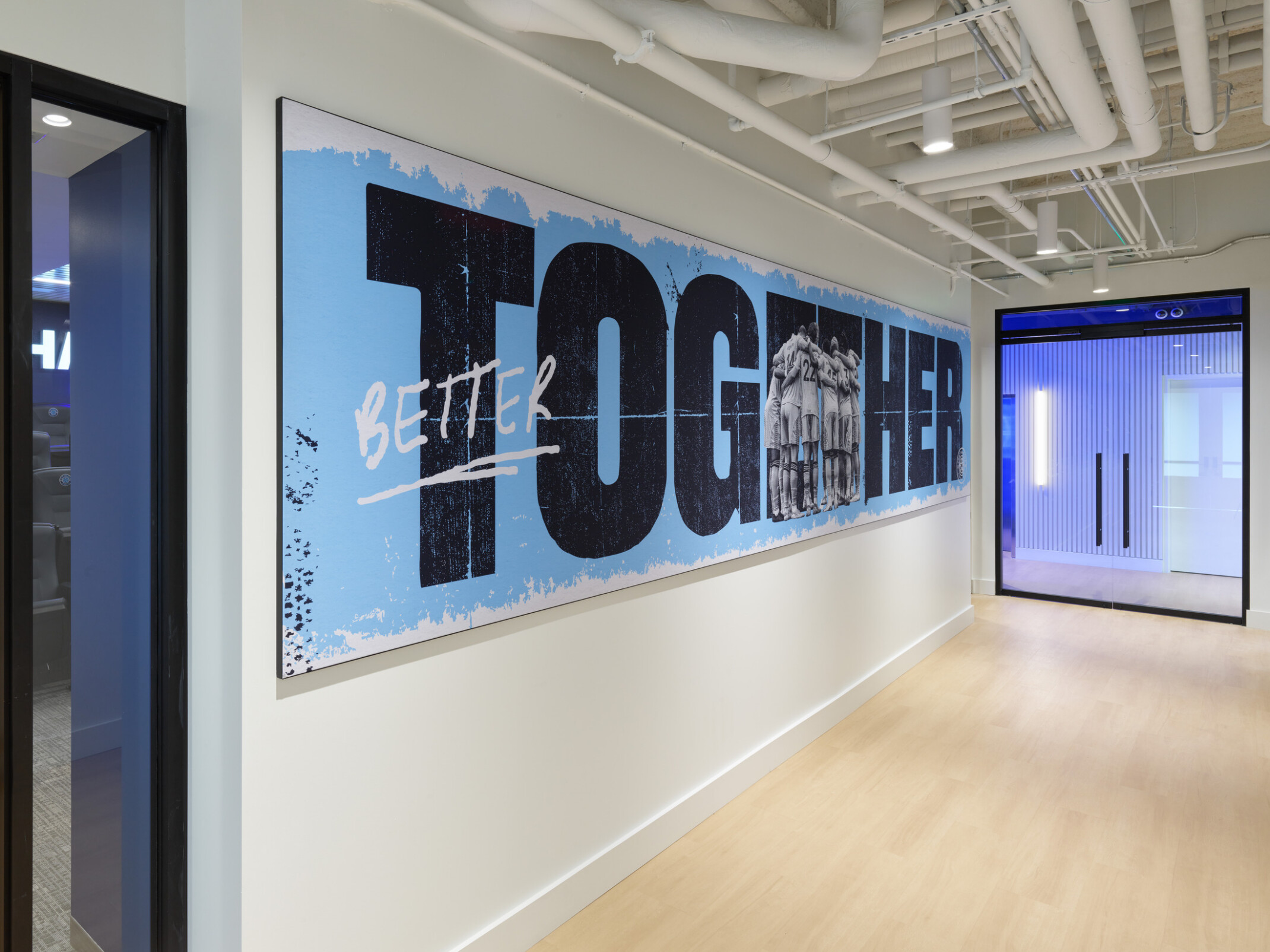 Large motivational wall graphic reading “BETTER TOGETHER” in a Chattanooga Football Club office hallway, featuring a team huddle image integrated into the lettering.