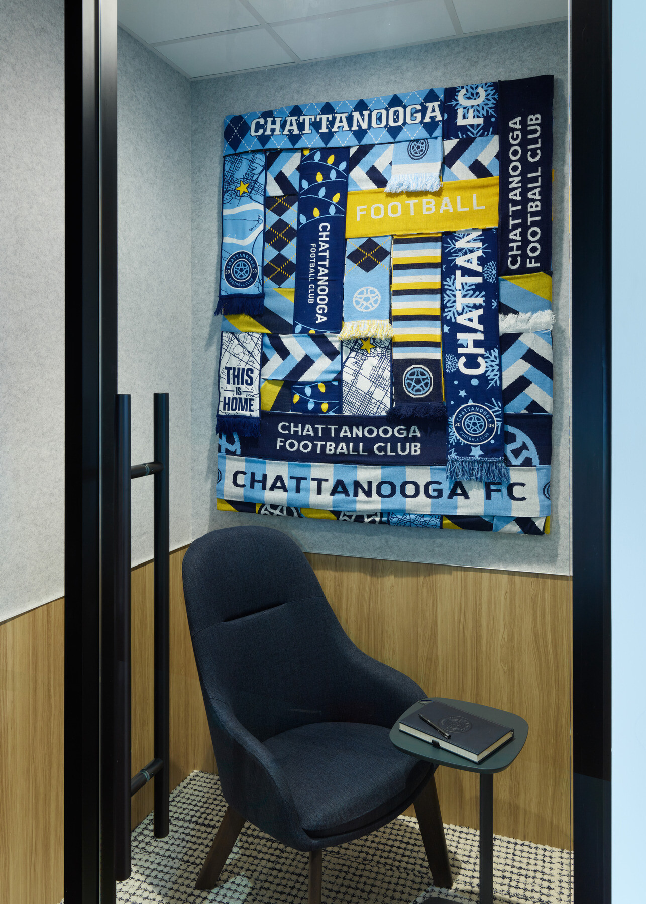 Small private meeting booth featuring a lounge chair, side table, and a decorative wall hanging made from Chattanooga Football Club scarves and branded textiles.
