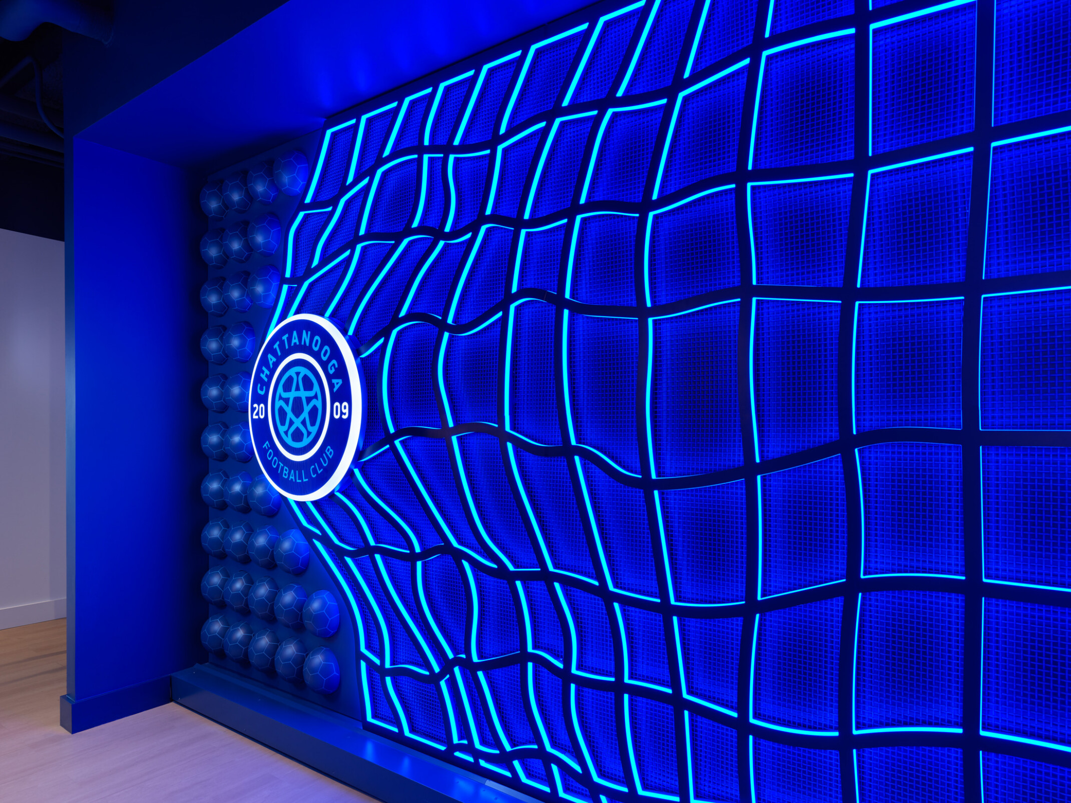 Large, illuminated Chattanooga Football Club logo mounted on a wall featuring a glowing blue soccer-net design and textured soccer-ball pattern accents