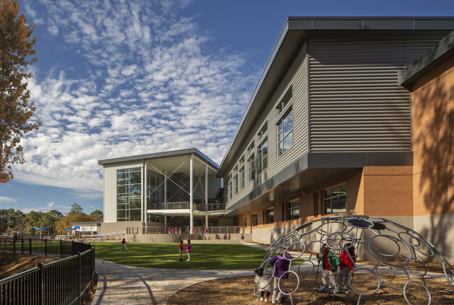 exterior photo of a school with green field and playground in the forefront of the recessed first floor building; multi-faceted and multi-colored building