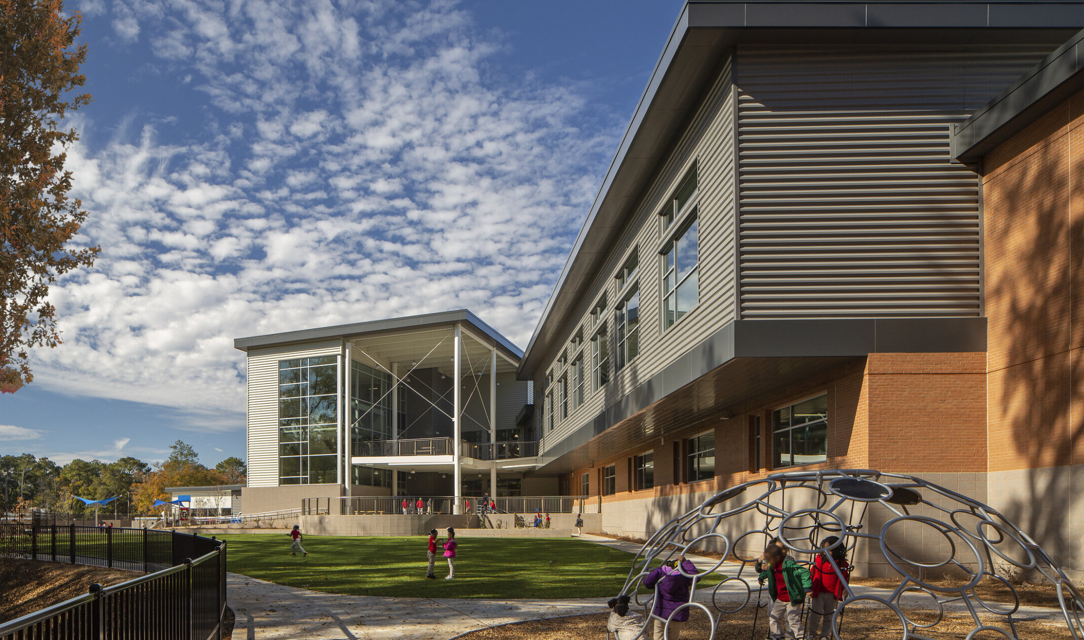 exterior photo of a school with green field and playground in the forefront of the recessed first floor building; multi-faceted and multi-colored building