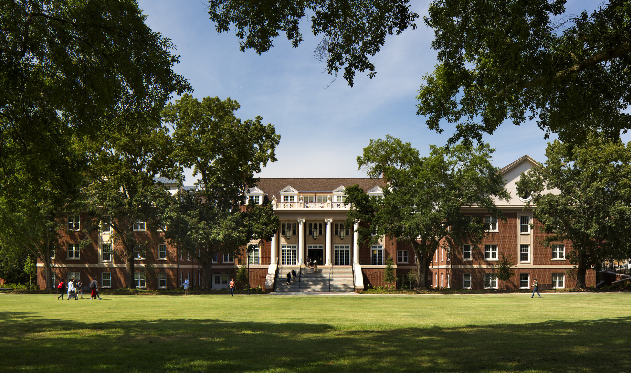 photo of a college building; classic brick and white column architecture surrounded by an expansive green quad