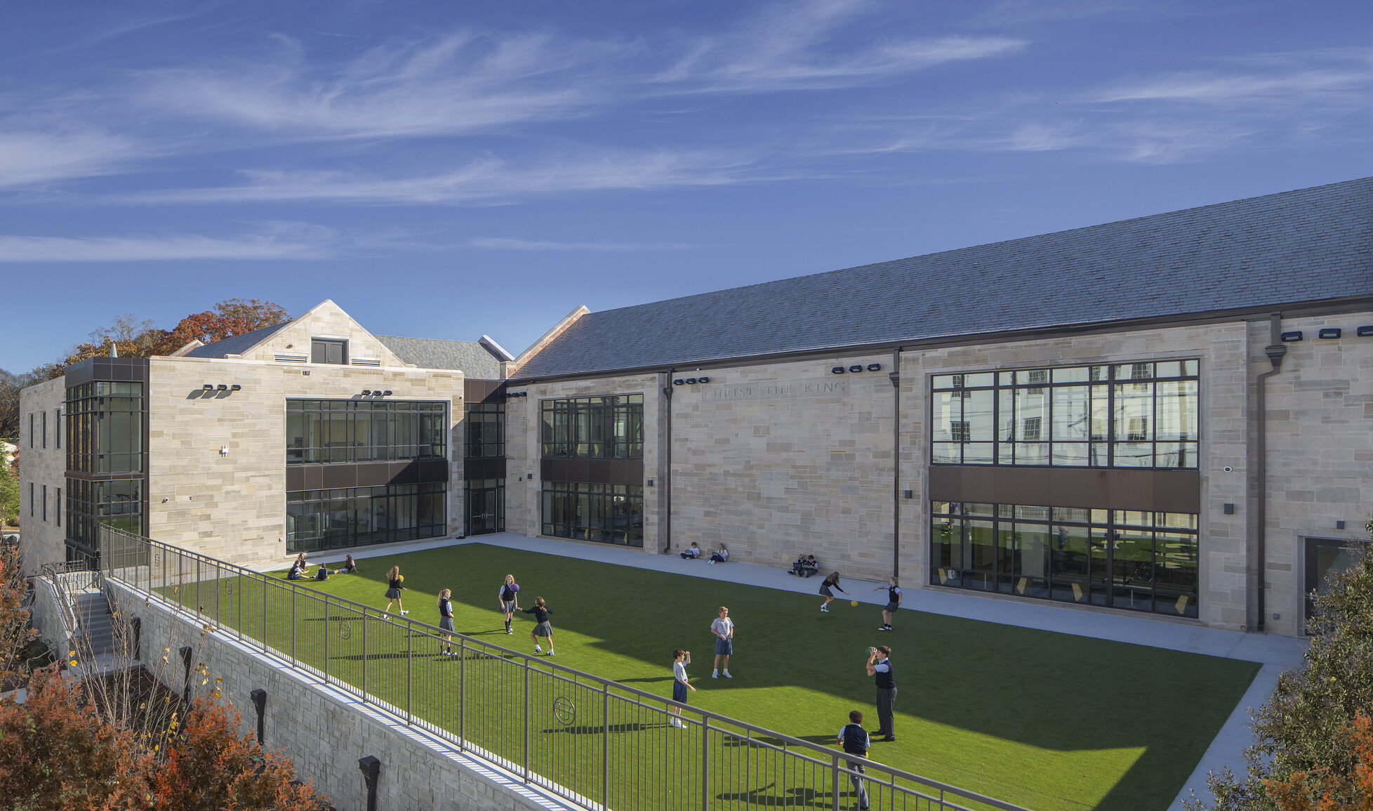 front exterior image of a modern higher education building; foreground turf field with children playing; multi-shaped facade