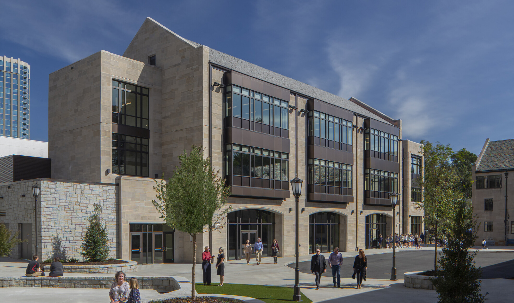 front exterior image of a modern higher education building; pavement and green courtyard for walking and sitting in the forefront of the building; multi-shaped facade