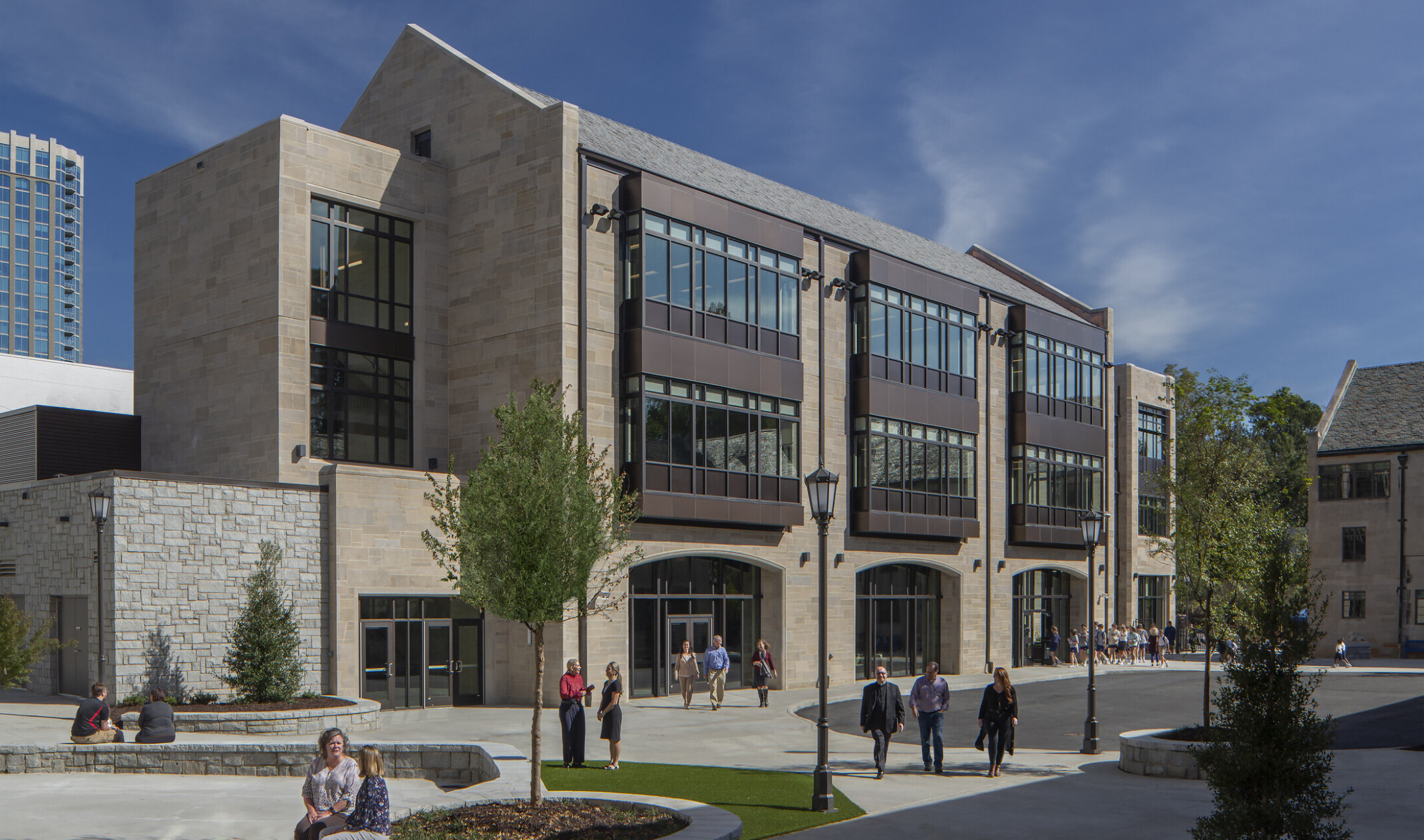 front exterior image of a modern higher education building; pavement and green courtyard for walking and sitting in the forefront of the building; multi-shaped facade