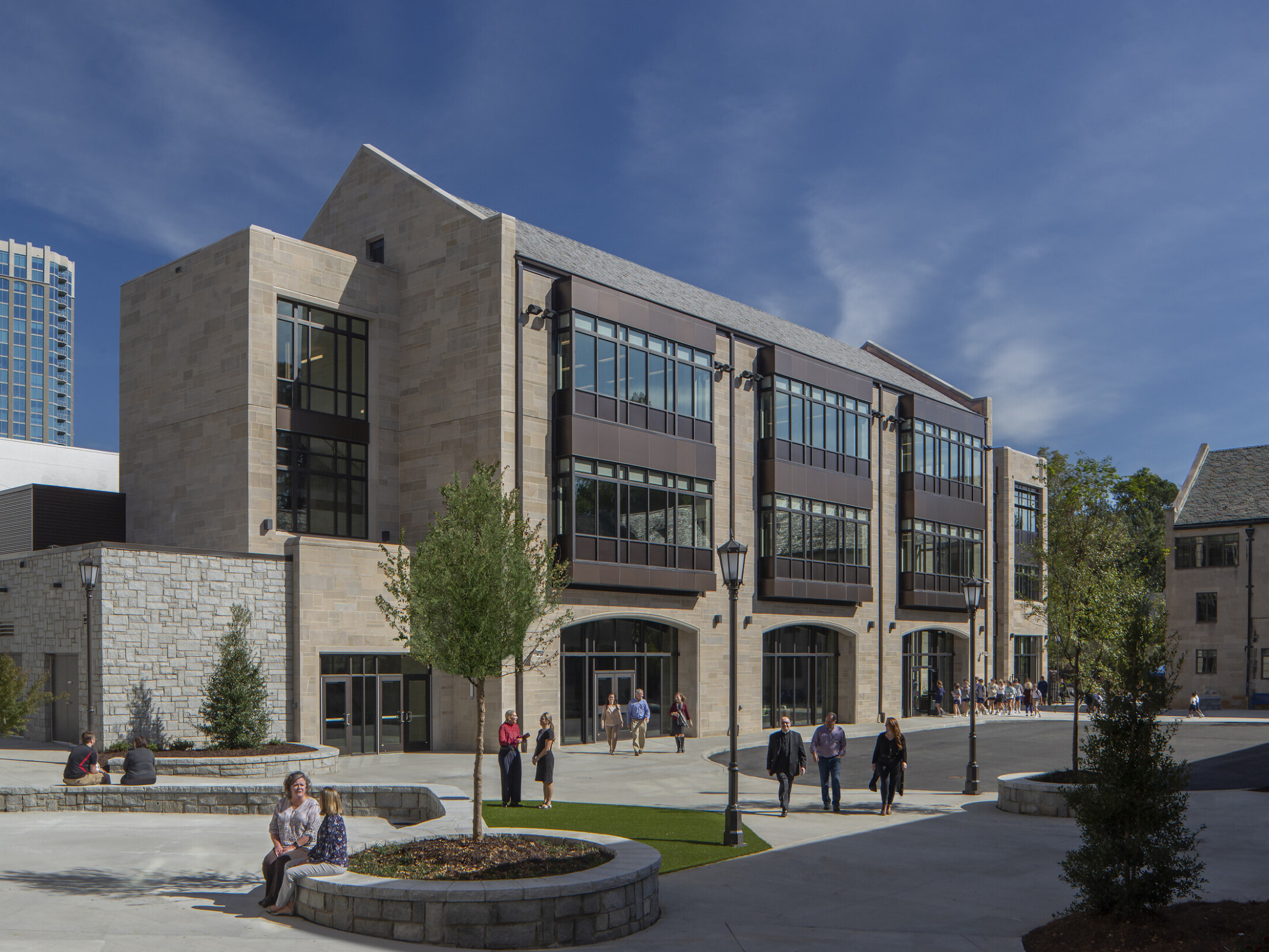 front exterior image of a modern higher education building; pavement and green courtyard for walking and sitting in the forefront of the building; multi-shaped facade