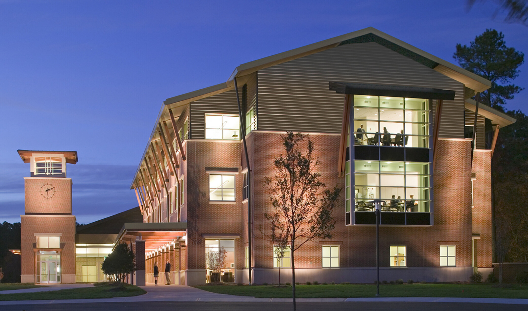evening image of a higher education space with interiors lit showing students studying at tables