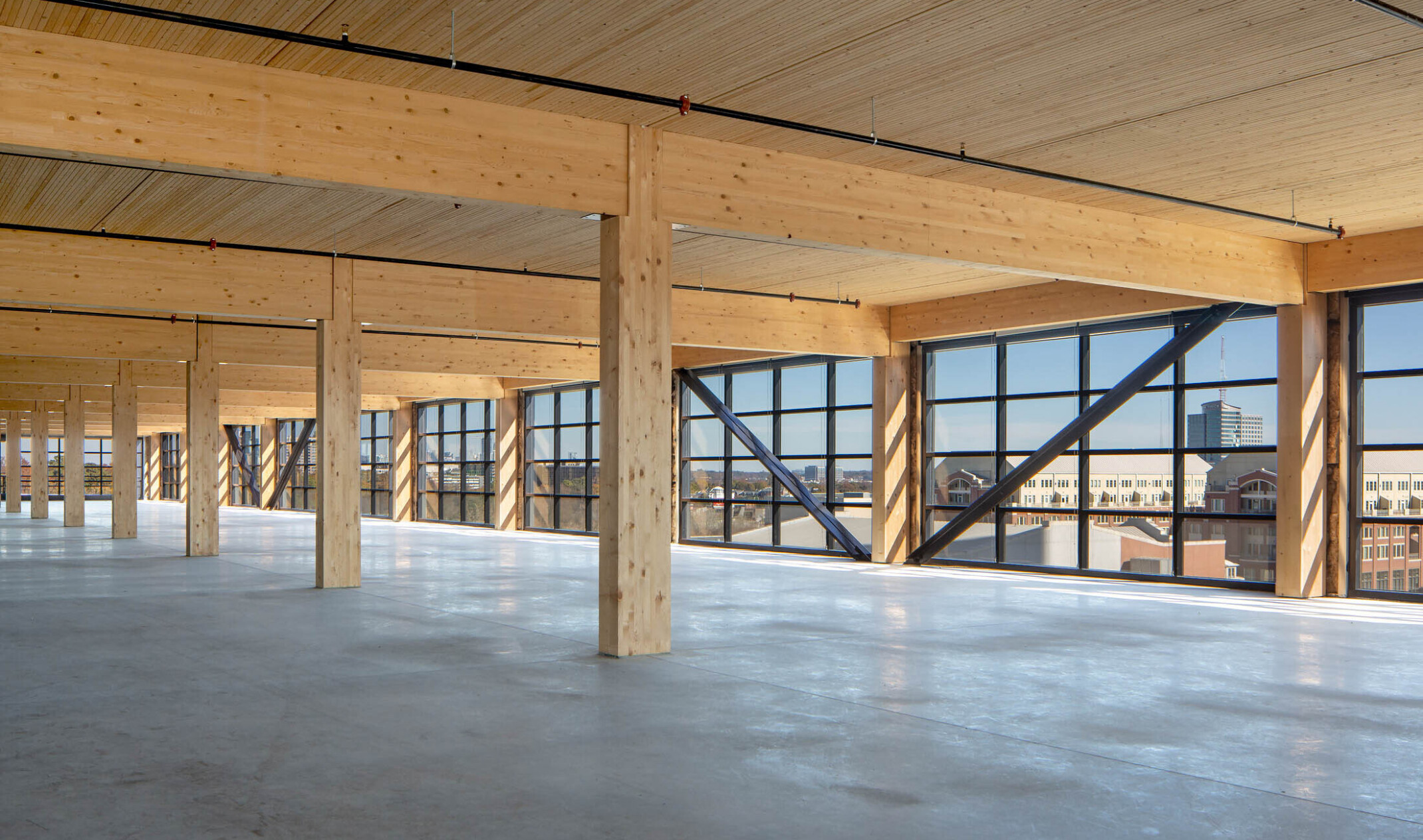 Interior with wood columns, ceiling and beams lined with floor to ceiling windows with black seams and exposed steel beams