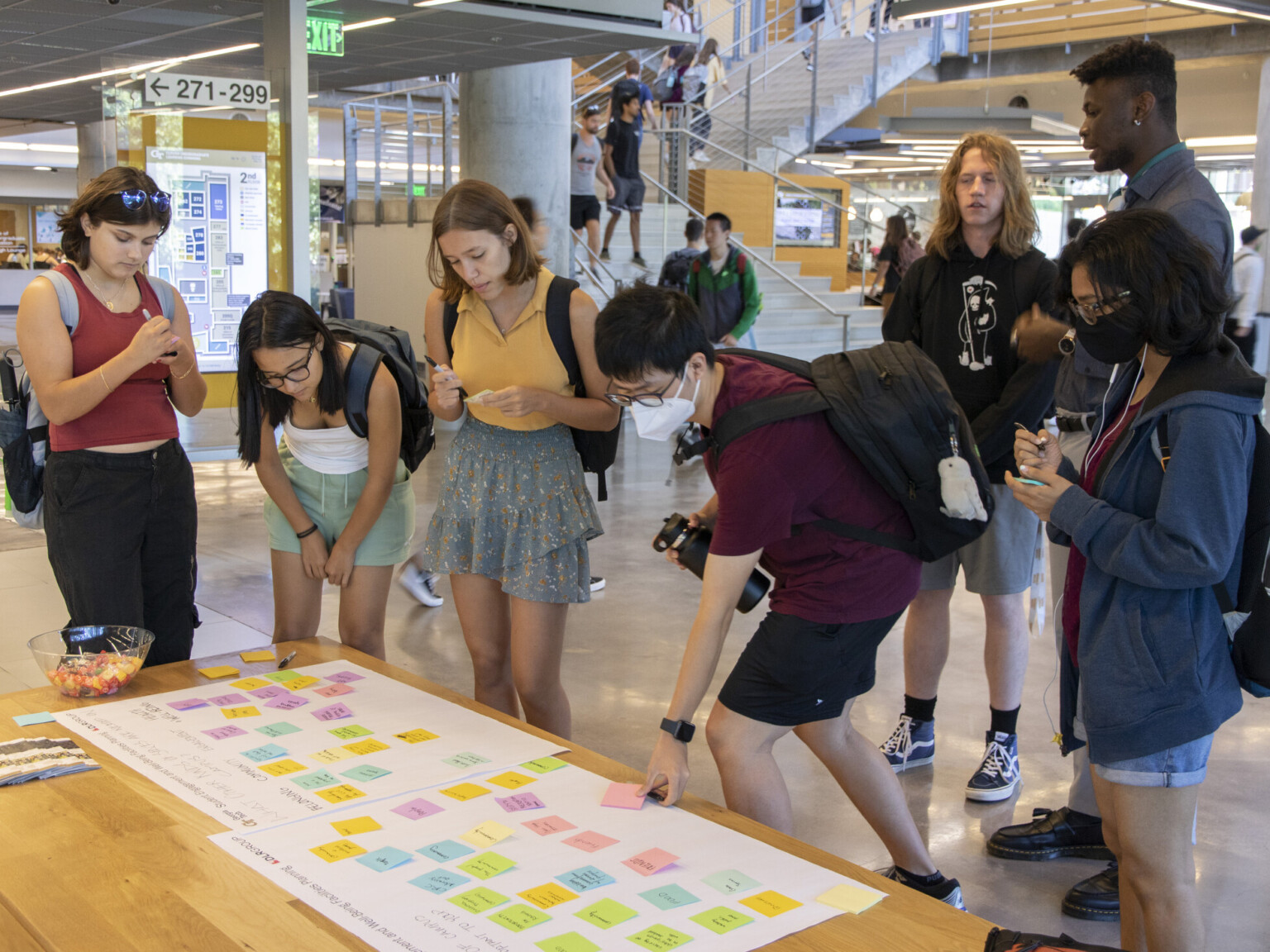Students interacting in a common area placing colorful sticky notes on white paper on a wooden table