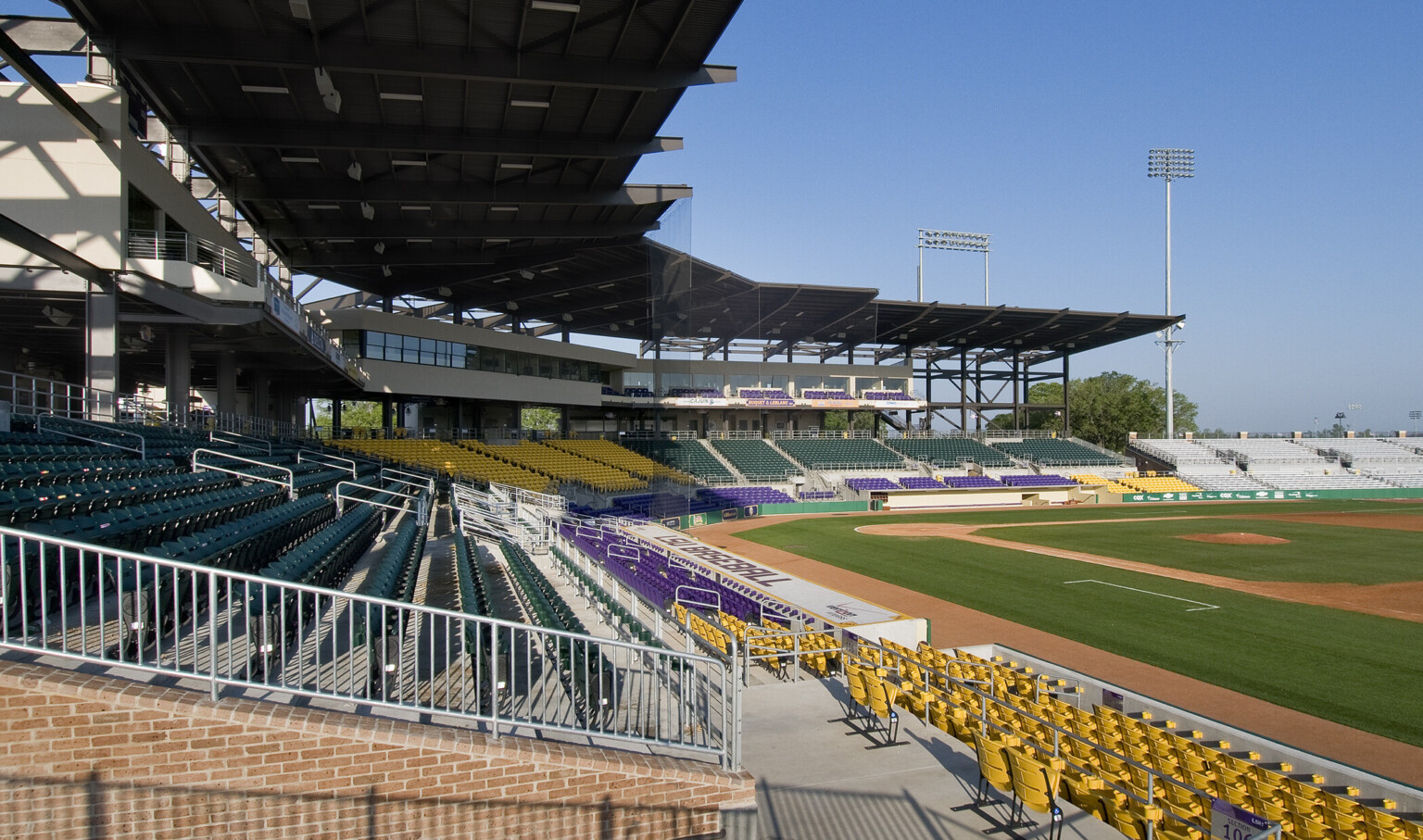 Black awning extends from boxes sheltering seats and supports net behind home plate. 1st baseline dugout labeled LSU Baseball