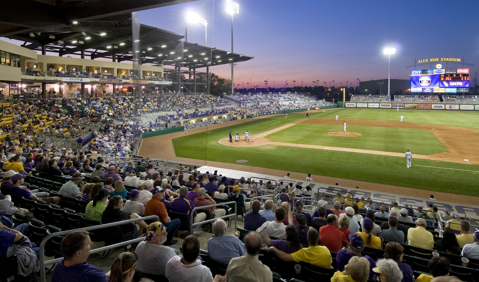 View from first base side across field. Lower deck seating behind left field with jumbotron display and stadium light above