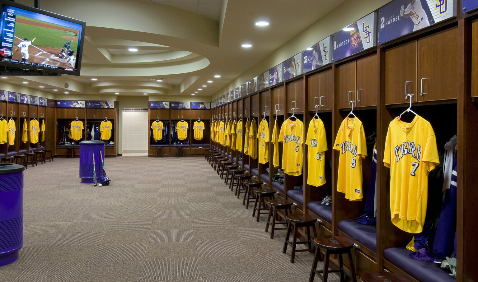 Locker room with wood cabinets above purple space for hanging gear. Yellow Jerseys hang in front of each, player's name above